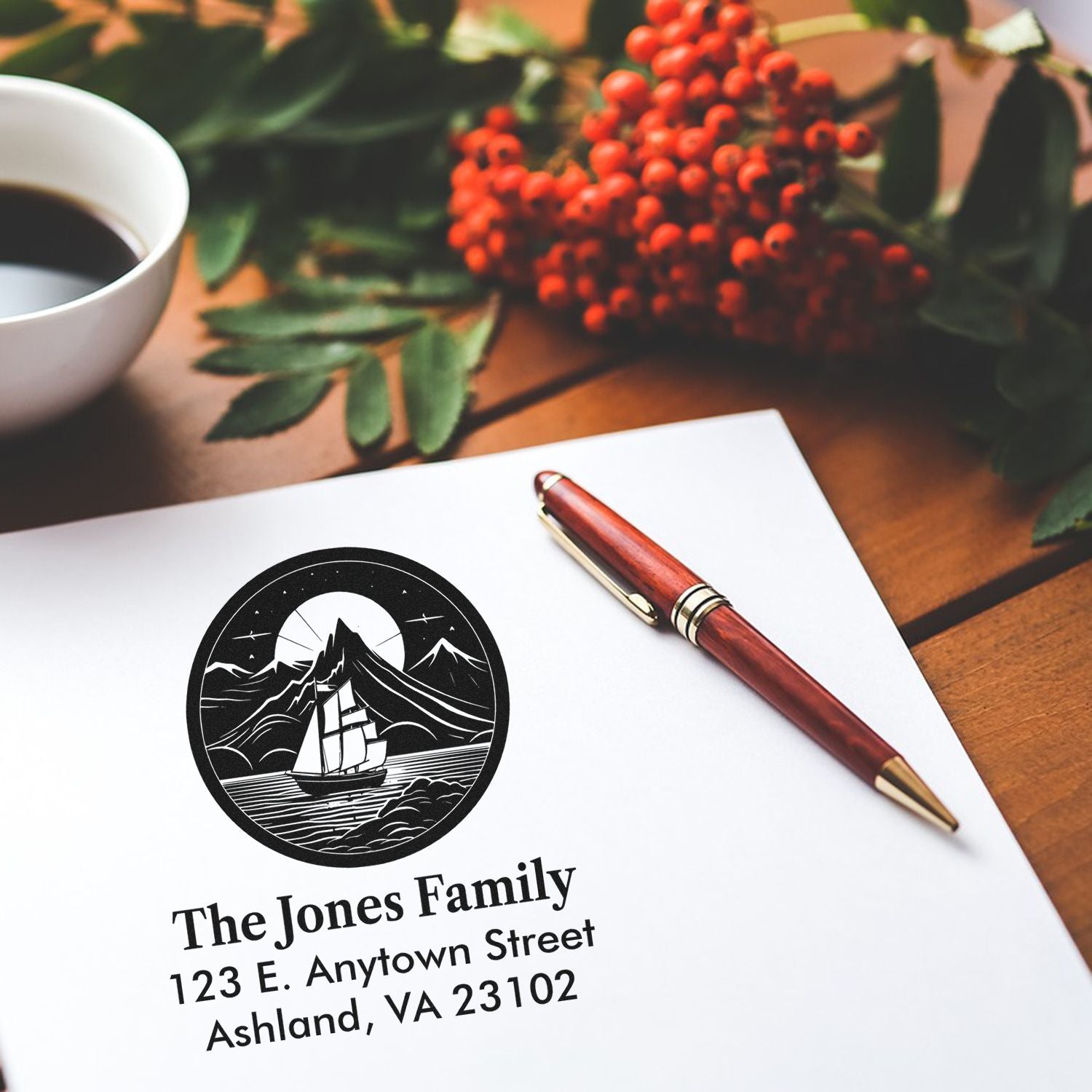 Custom return address rubber stamp with sailboat mountain logo on personalized stationery beside a pen and coffee.