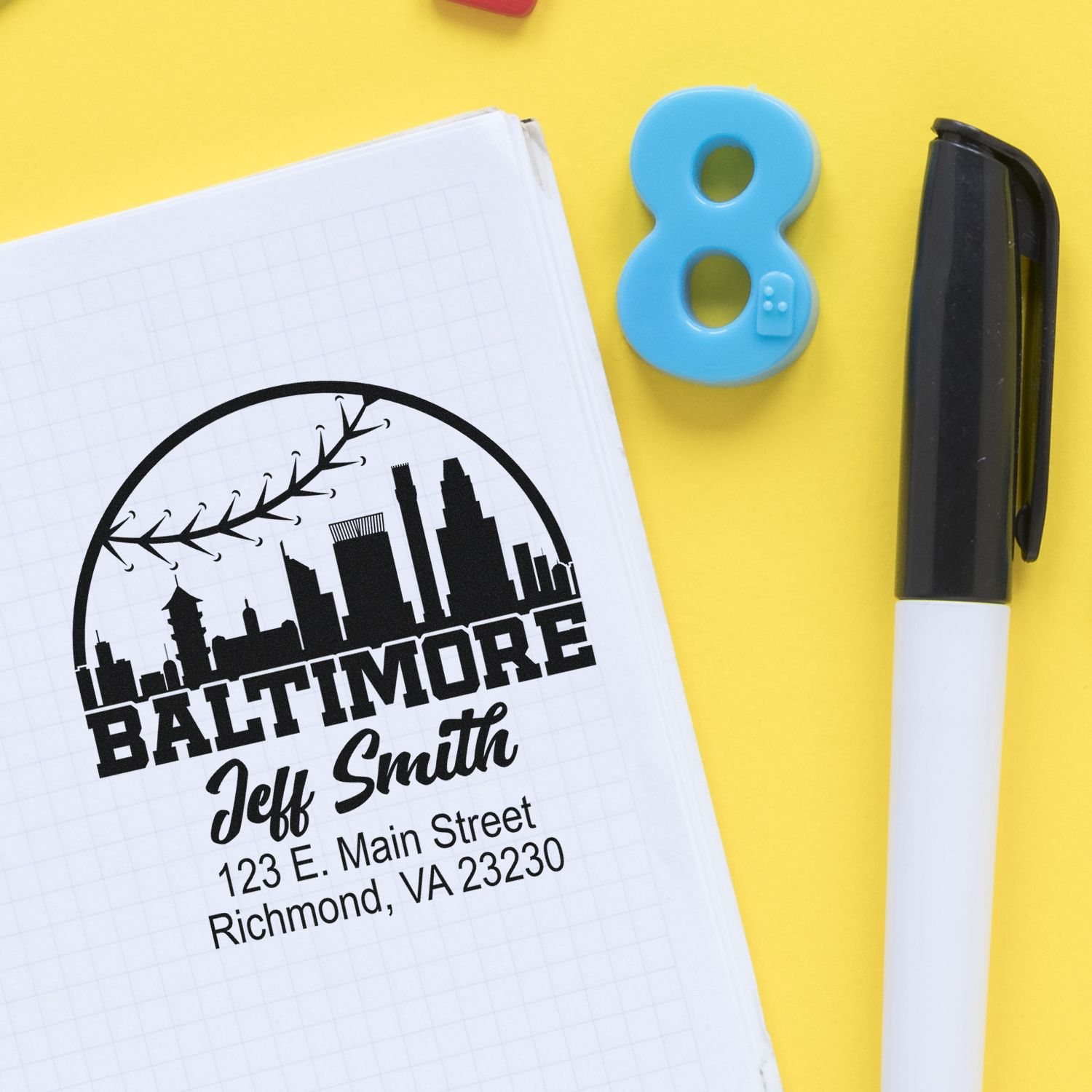 Personalized Baltimore rubber stamp with skyline logo, name, and address on notebook beside a marker.