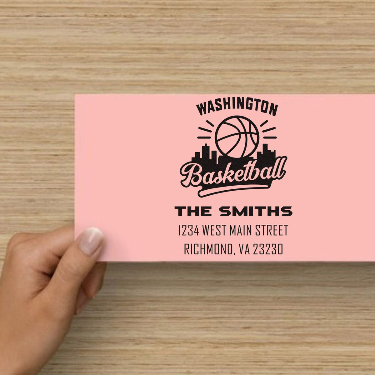 Personalized rubber stamp for Washington Basketball mailers, featuring The Smiths family name and address on a pink envelope.