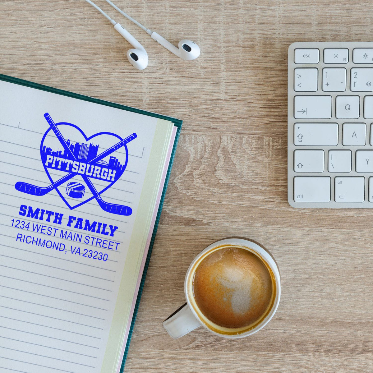Custom rubber stamp impression with Pittsburgh hockey heart design and Smith Family address on notebook, beside coffee and keyboard.