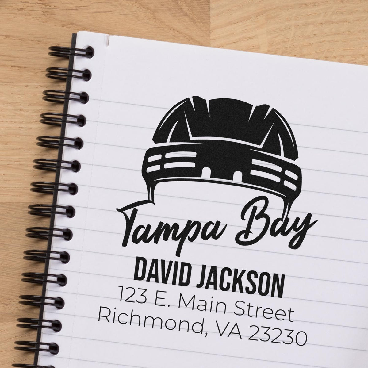 Custom rubber stamp mockup with Tampa Bay logo, name, and return address on a spiral notebook.