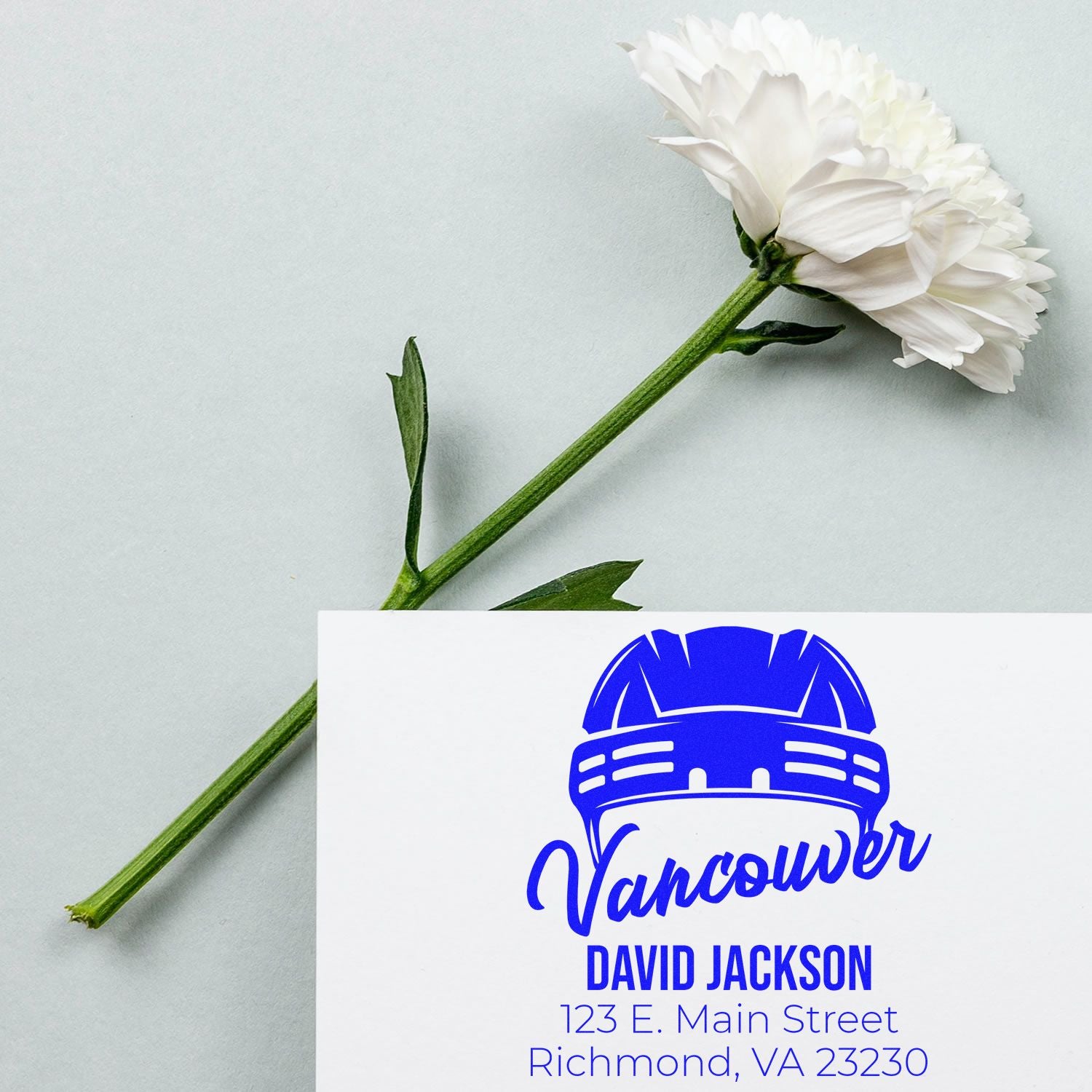 Custom rubber stamp business card with blue Vancouver logo, name, and address beside a white flower.