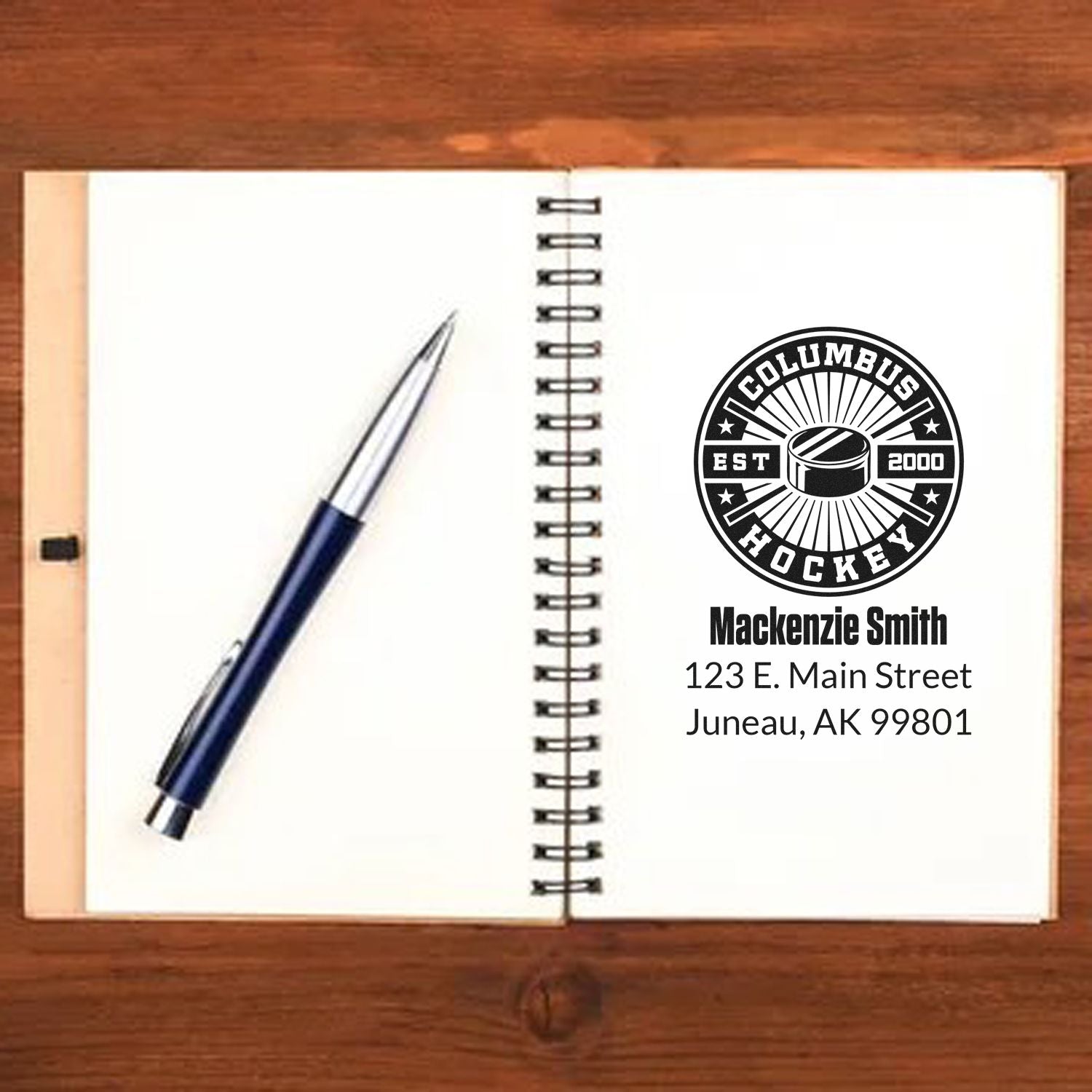 Custom hockey rubber stamp mockup with name and Juneau, AK address on an open notebook for personalized branding.