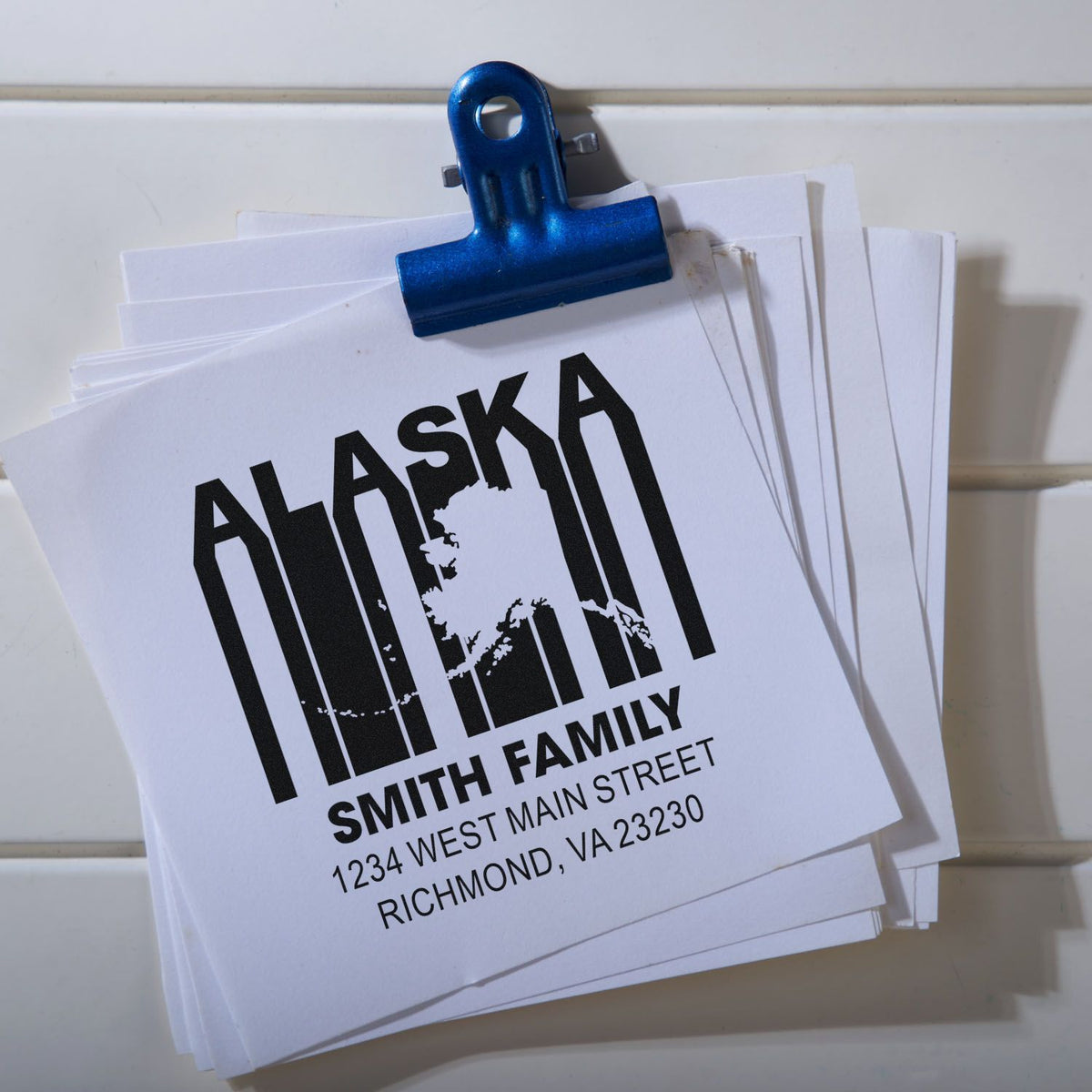 Custom Alaska family return address rubber stamp design on stacked paper sheets with name and mailing address.