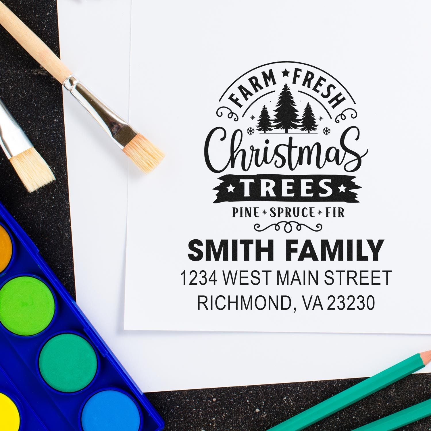 Custom rubber stamp design with Farm Fresh Christmas Trees, Smith Family name, and address, shown with paintbrushes and paint palette.