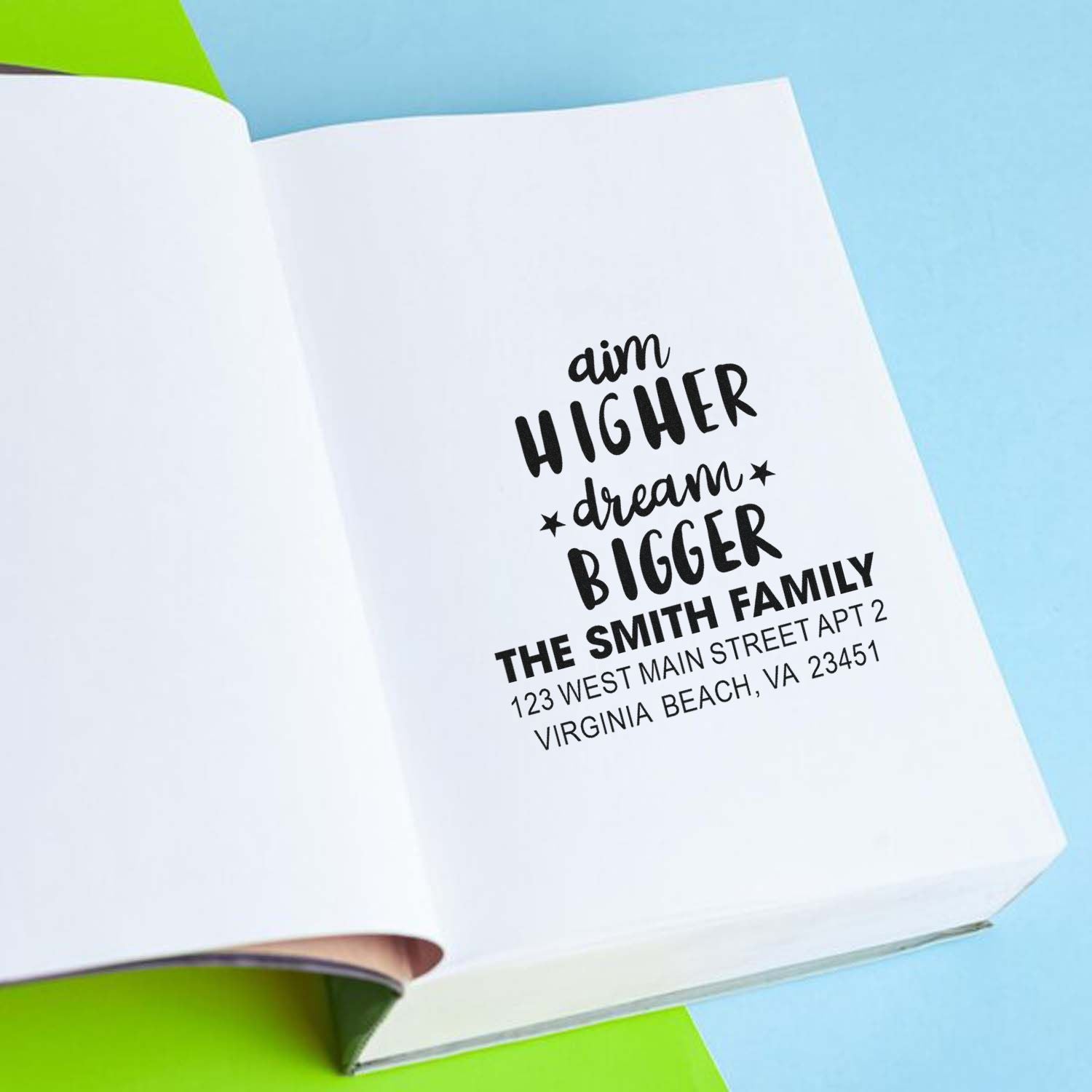 Personalized rubber return address stamp with aim higher dream bigger design on an open notebook for family mail.