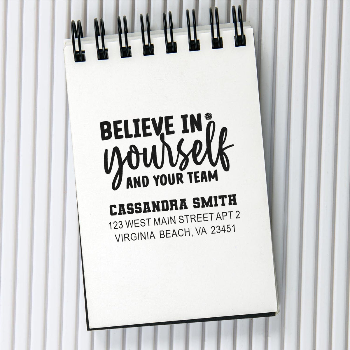 Personalized rubber stamp impression on spiral notebook with motivational quote and return address.