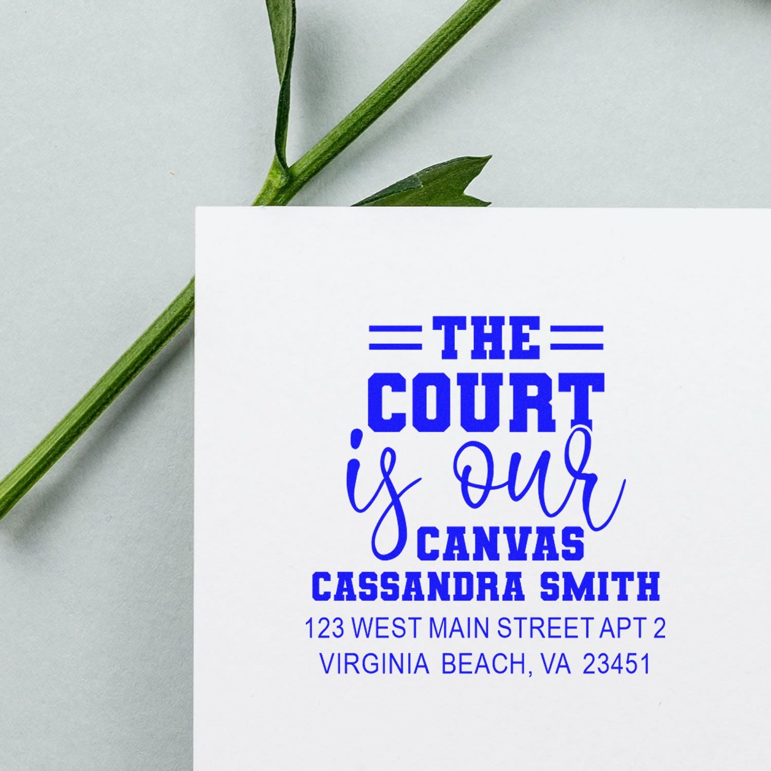 Custom rubber stamp impression with The Court Is Our Canvas, name, and address in blue ink on white paper.