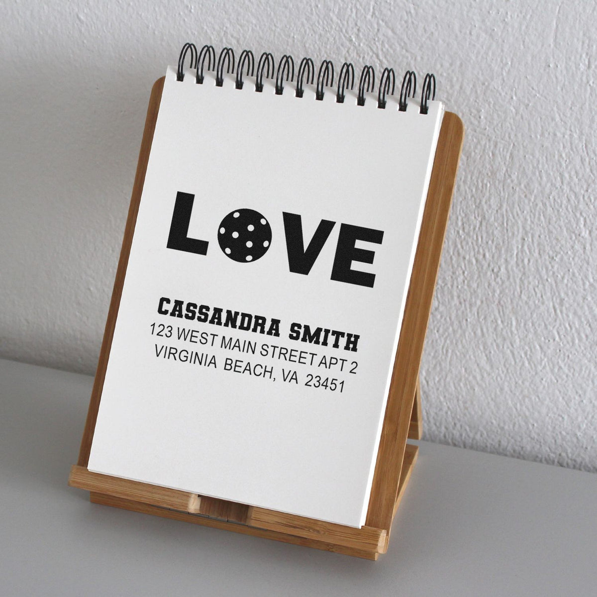 Custom rubber stamp design with LOVE and personalized name and address, shown on a notebook display stand.