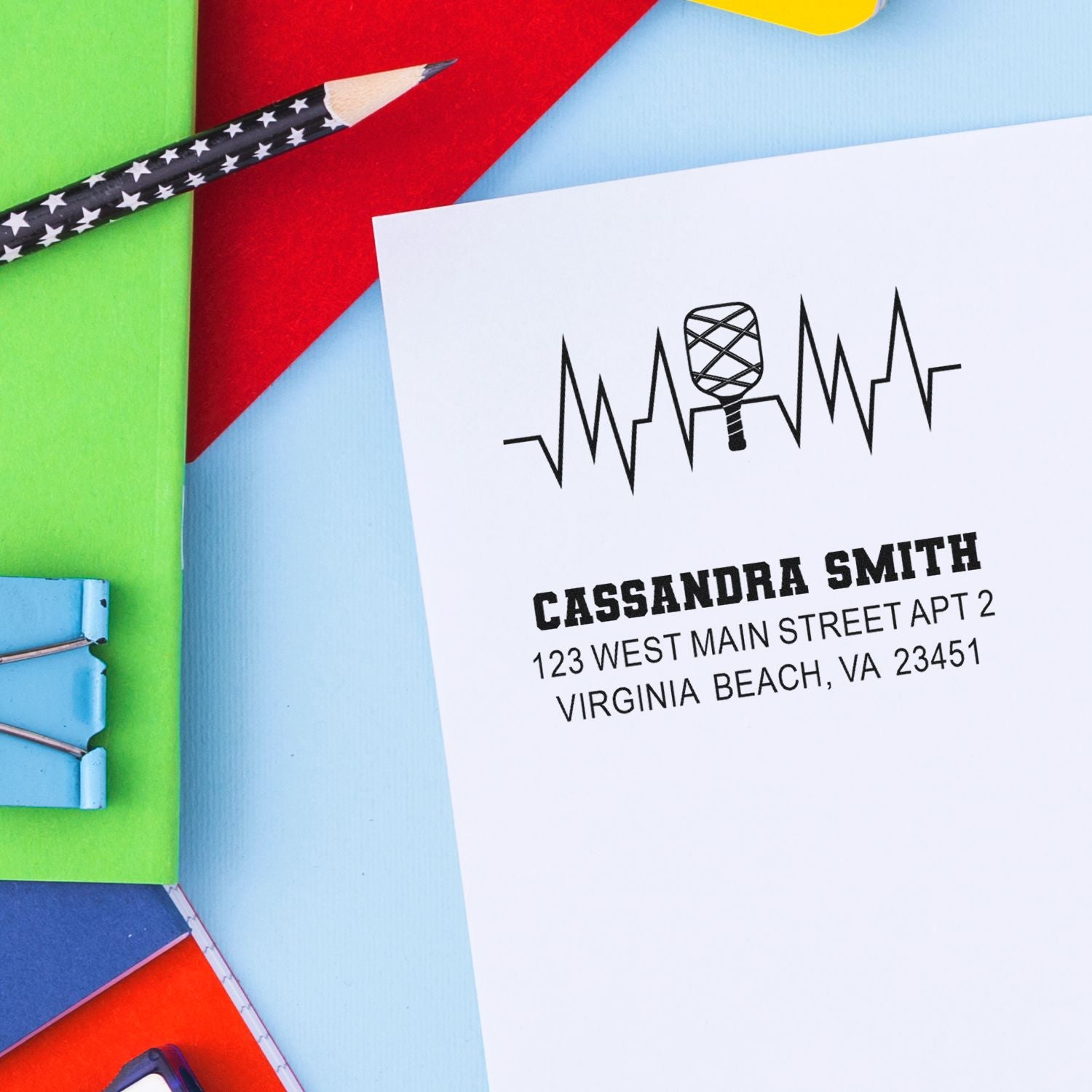 Custom rubber address stamp design with name and Virginia Beach address on white paper, shown with colorful stationery.