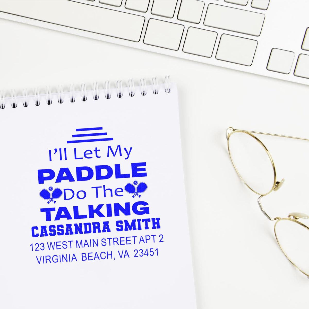 Blue custom rubber stamp with name and address, reading Ill Let My Paddle Do The Talking on a notebook.