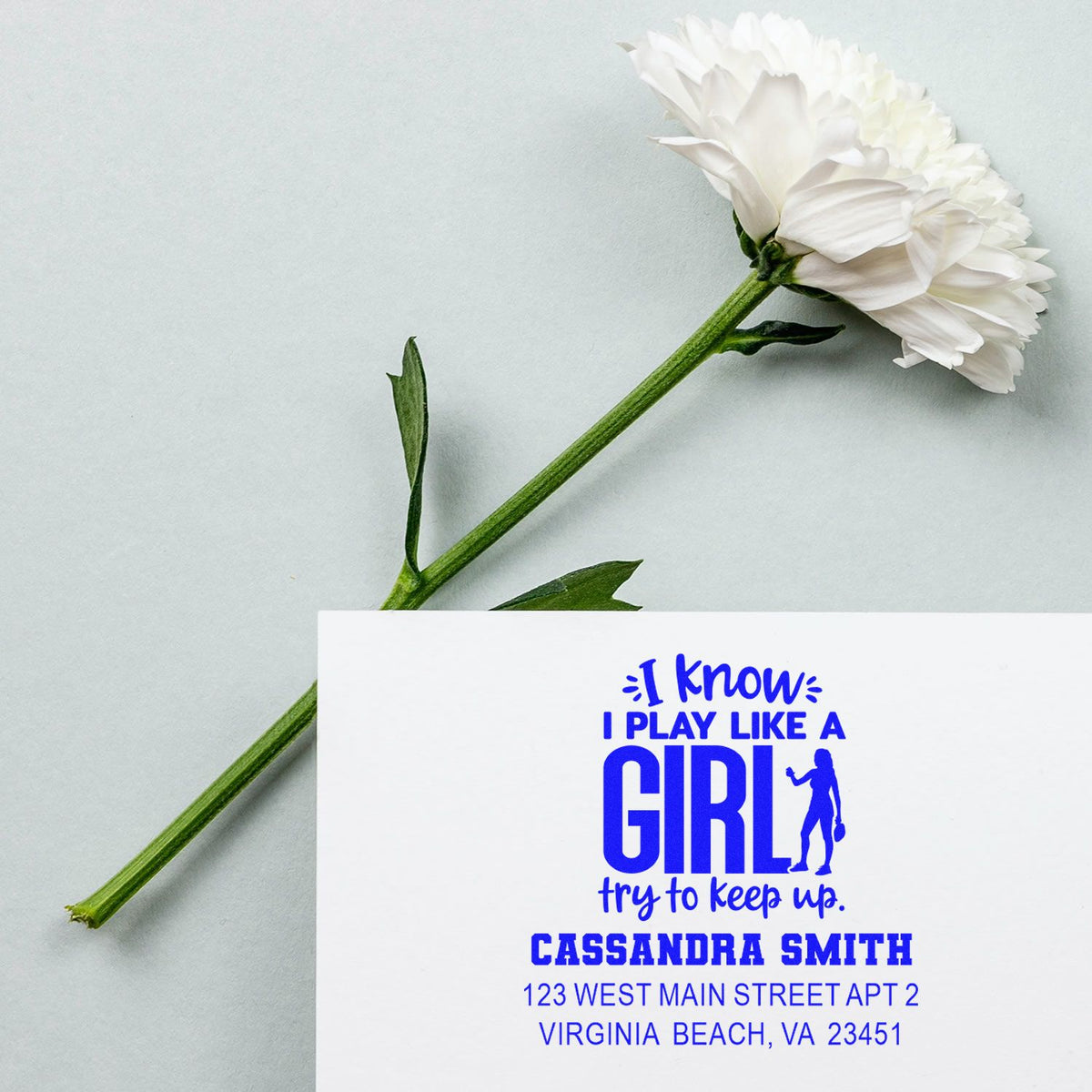 Custom rubber address stamp with bold blue I play like a girl design, showing a personalized mailing imprint on a card.