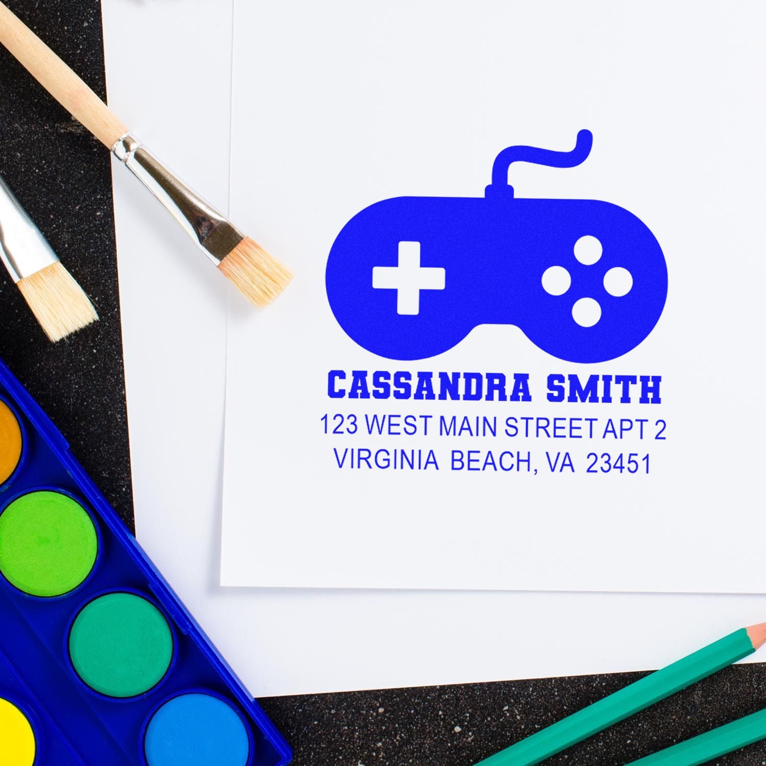 Custom rubber address stamp design with game controller icon for Cassandra Smith, Virginia Beach, shown with craft supplies.