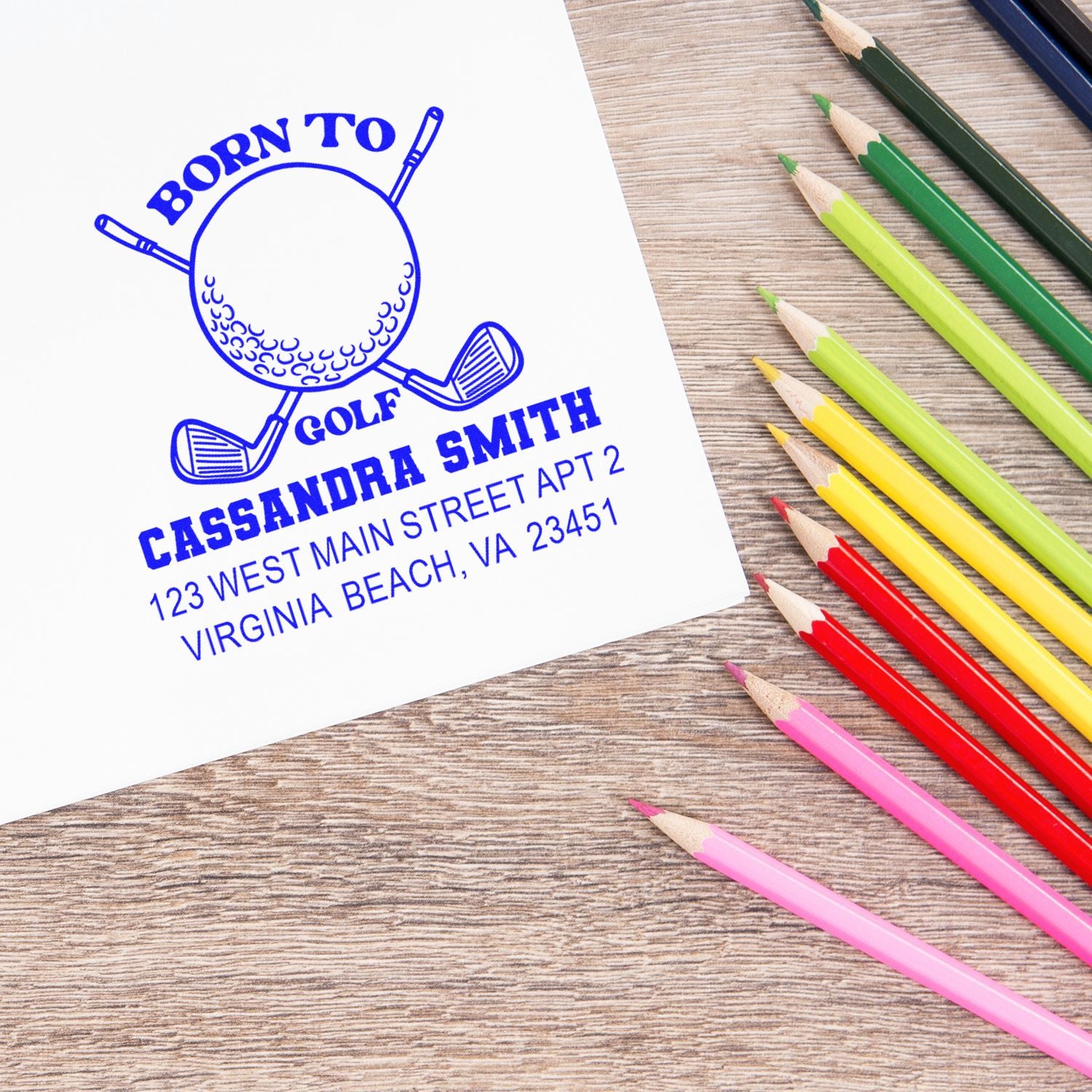 Custom golf rubber stamp with personalized name and return address, shown on paper beside colored pencils.