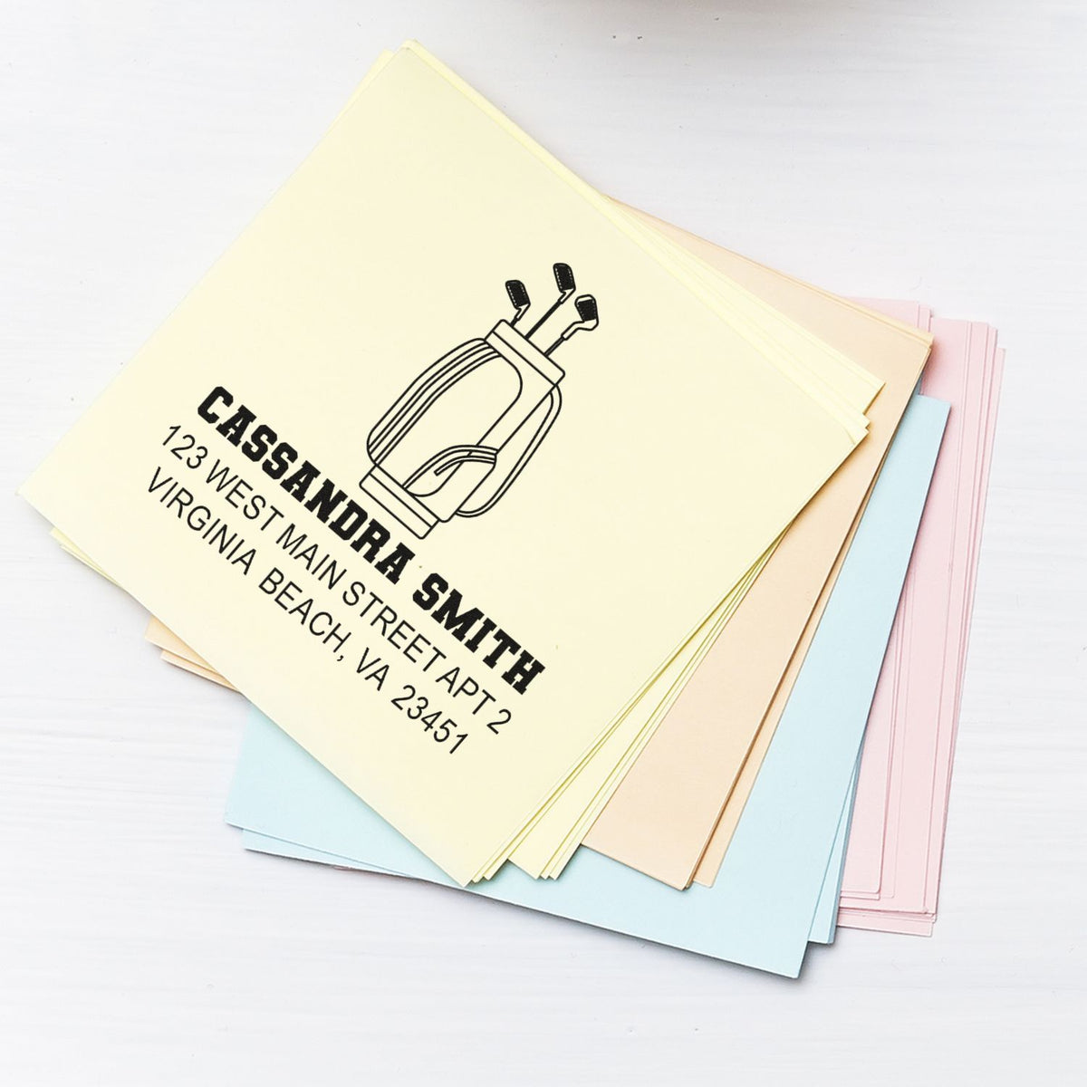 Custom return address rubber stamp for Cassandra Smith with golf club logo, shown on pastel paper samples.