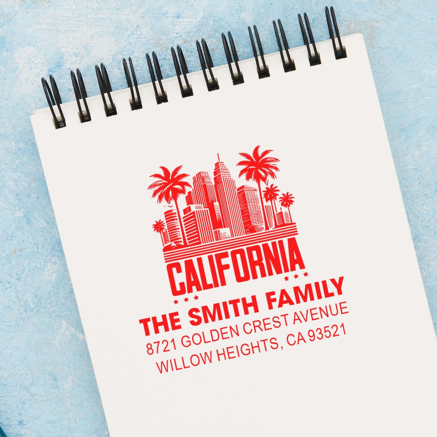 Custom California address rubber stamp with skyline and palm trees, personalized for The Smith Family on a notebook.