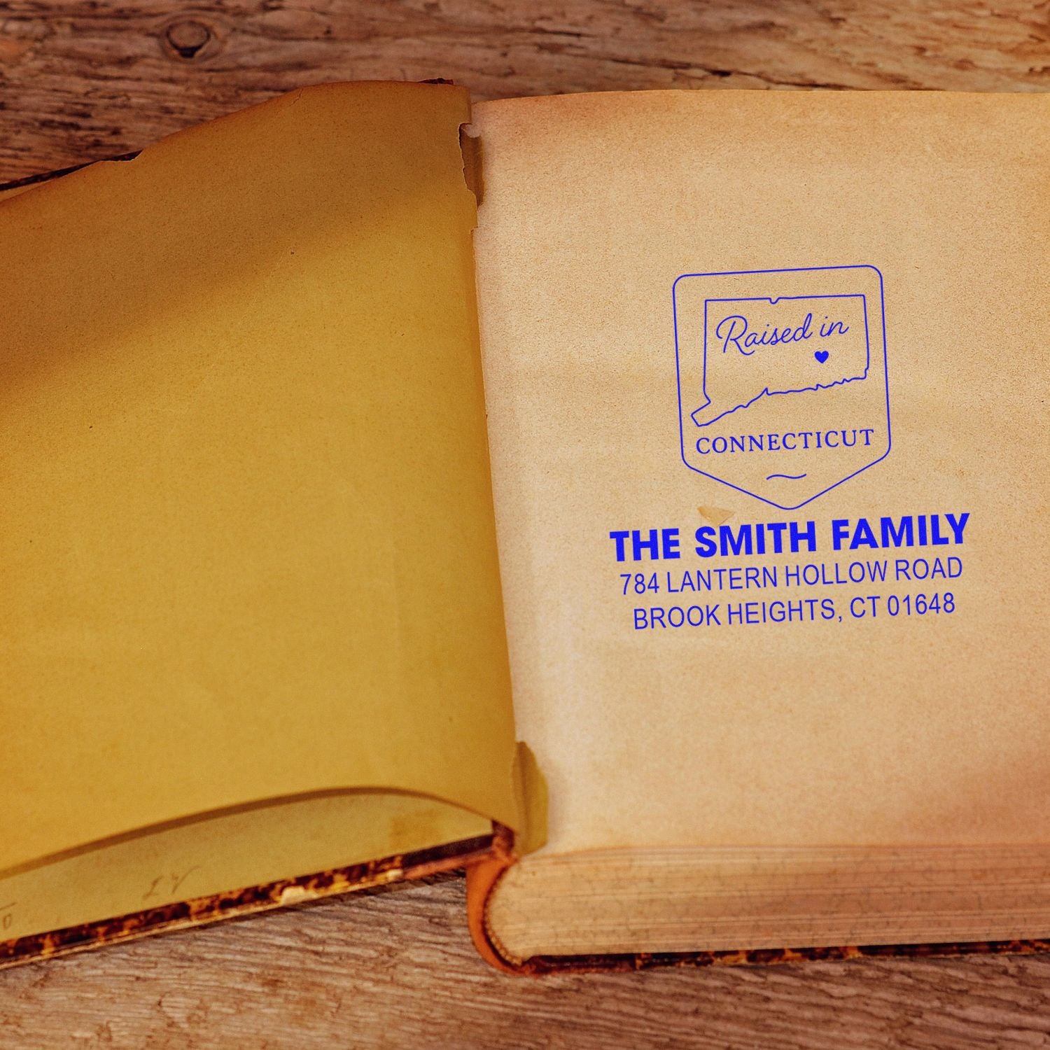 Custom raised in Connecticut rubber address stamp on an open book page, featuring family name and mailing address.