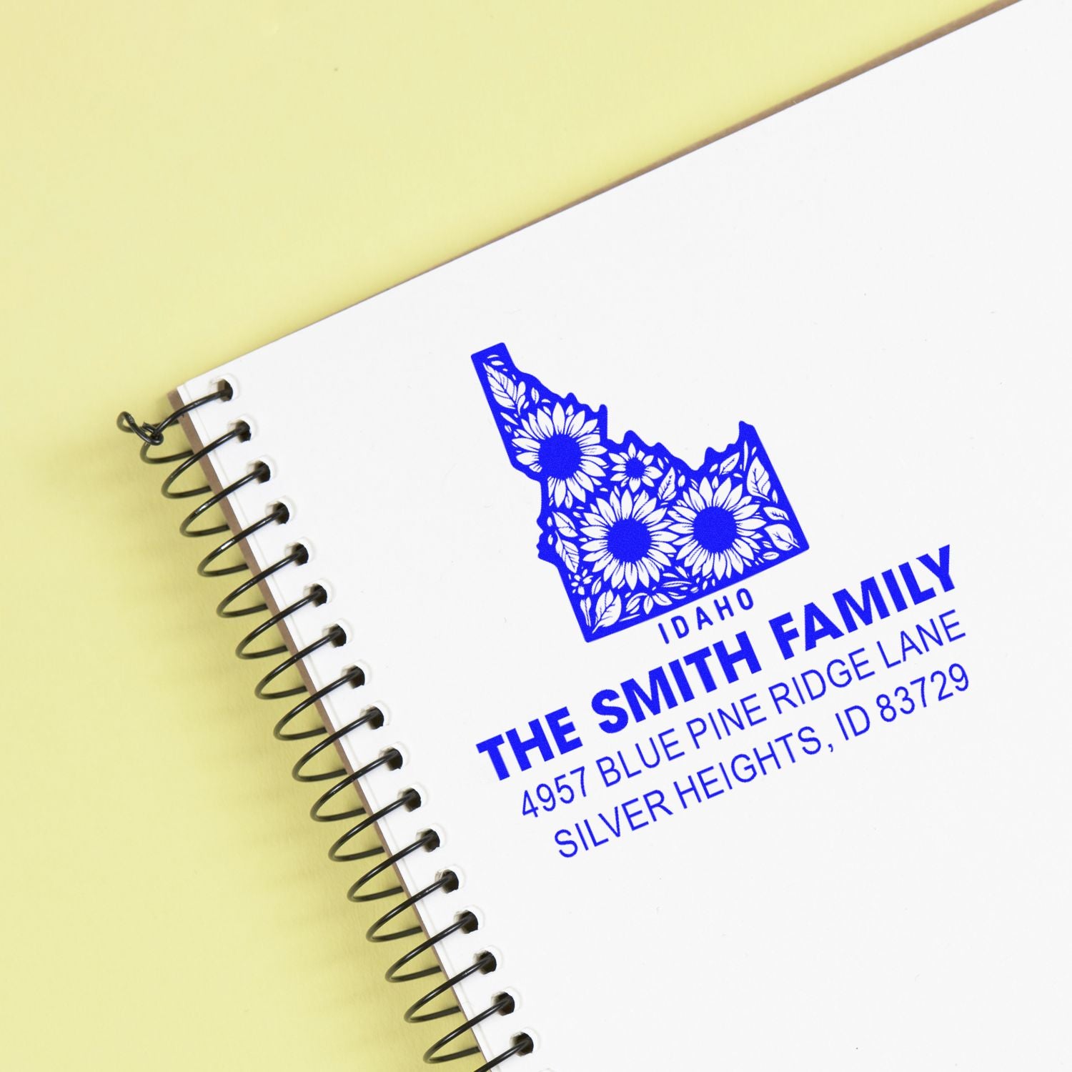 Custom blue Idaho family address rubber stamp on a spiral notebook, featuring a floral state design and return address.