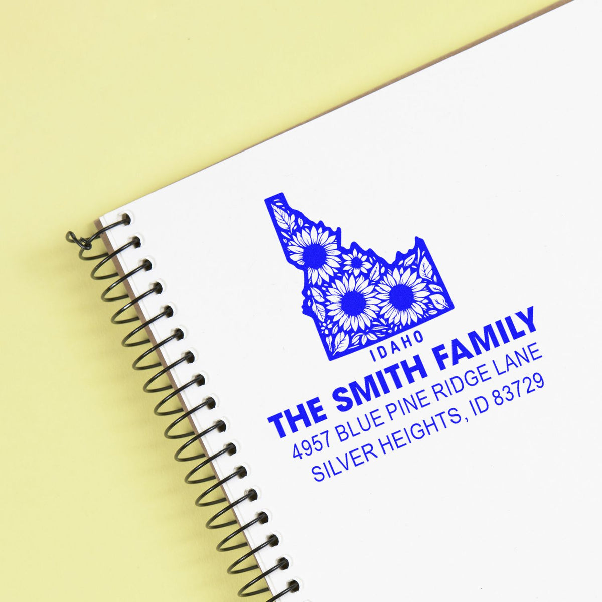 Blue custom Idaho family address rubber stamp with floral state design on a spiral notebook