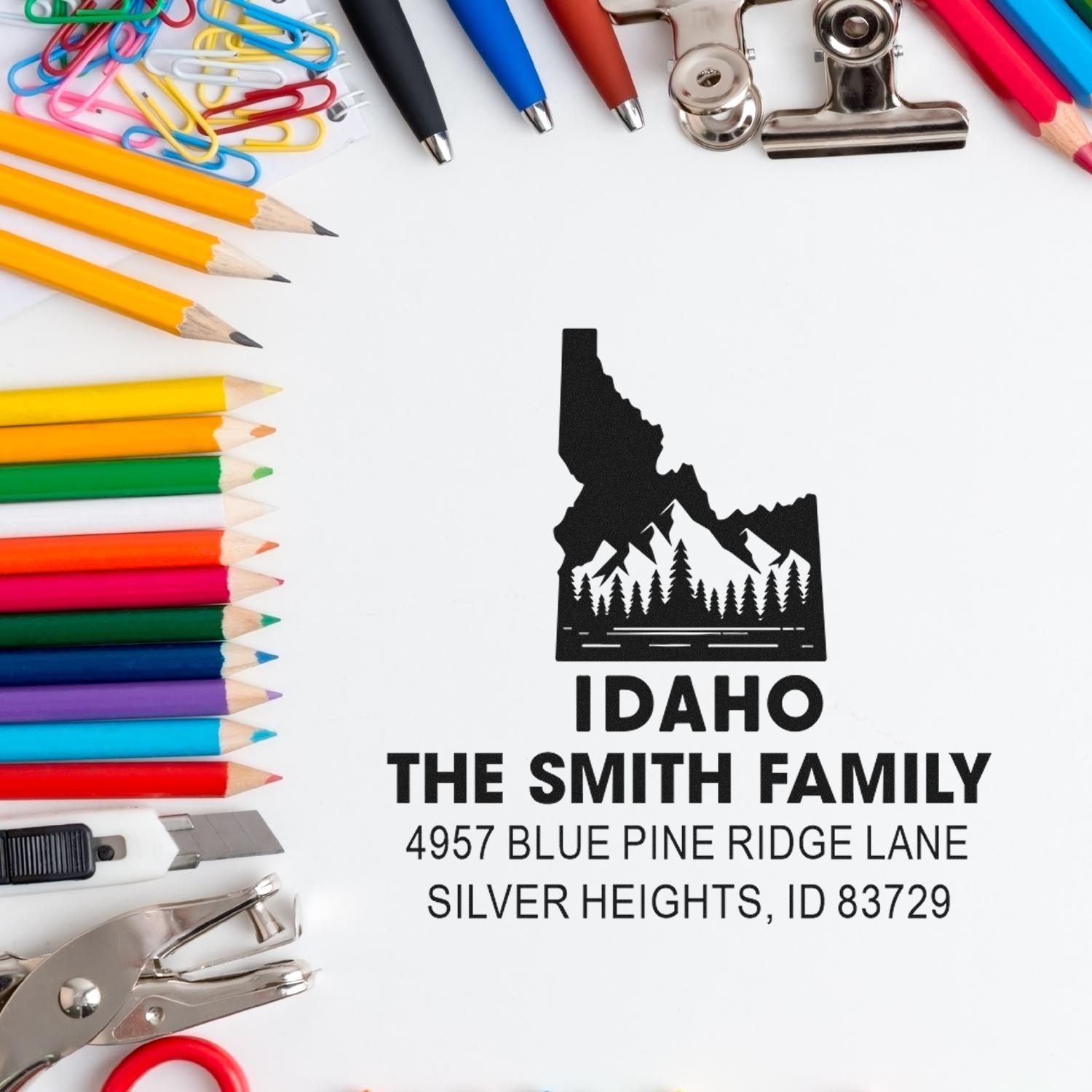 Custom Idaho return address rubber stamp with mountain design, surrounded by pencils, pens, and office stationery.
