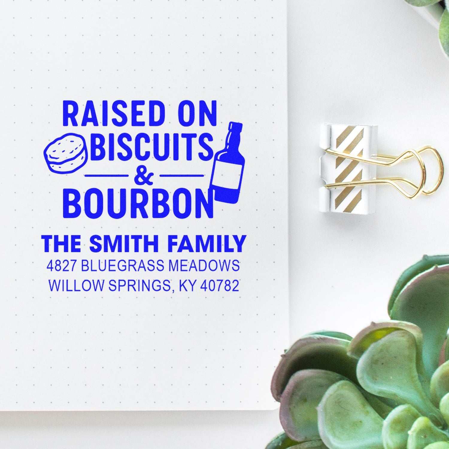 Custom rubber stamp imprint reading Raised on Biscuits & Bourbon with family name and address on a notebook page.