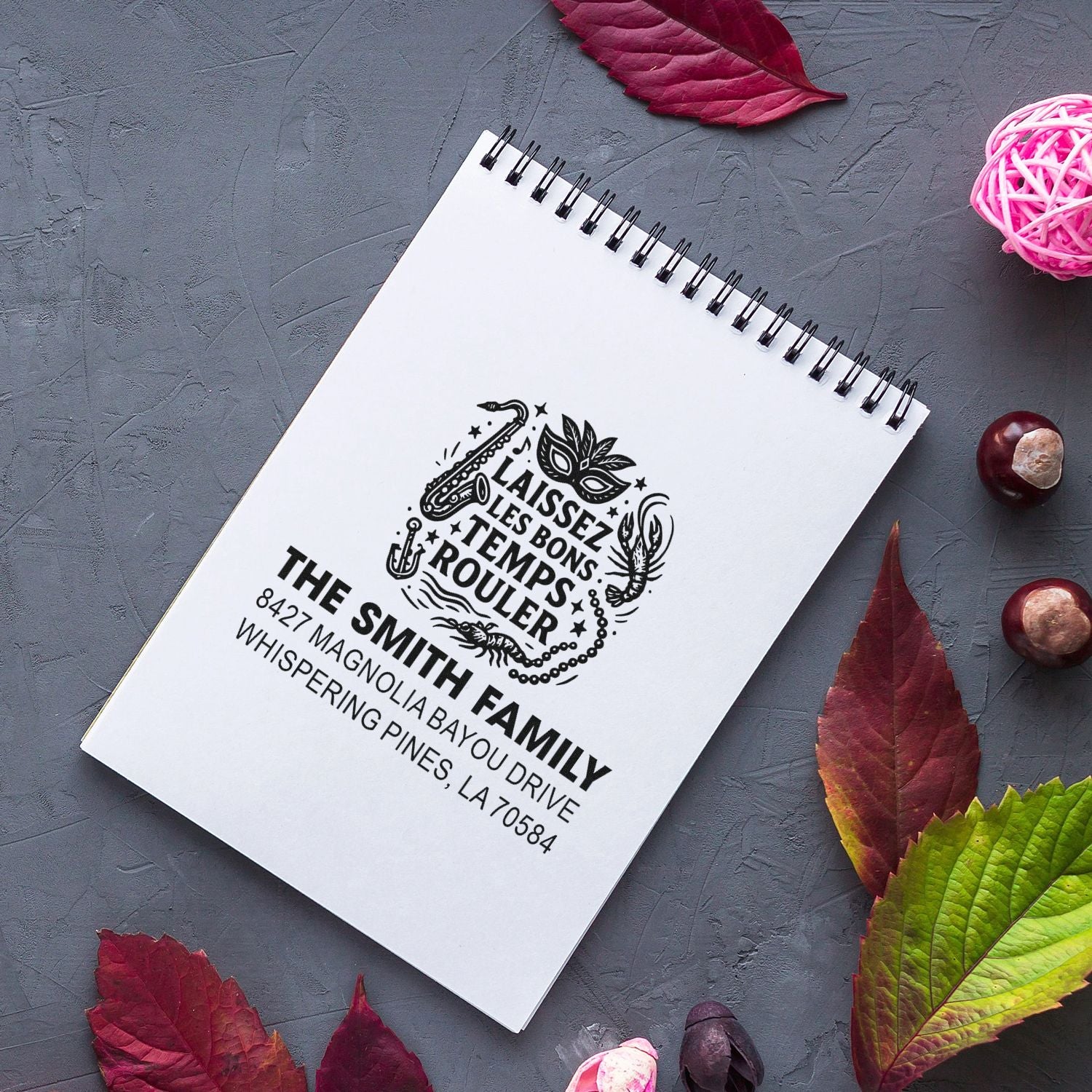 Custom rubber stamp with personalized family return address and Mardi Gras design on notebook, for stationery and packaging.