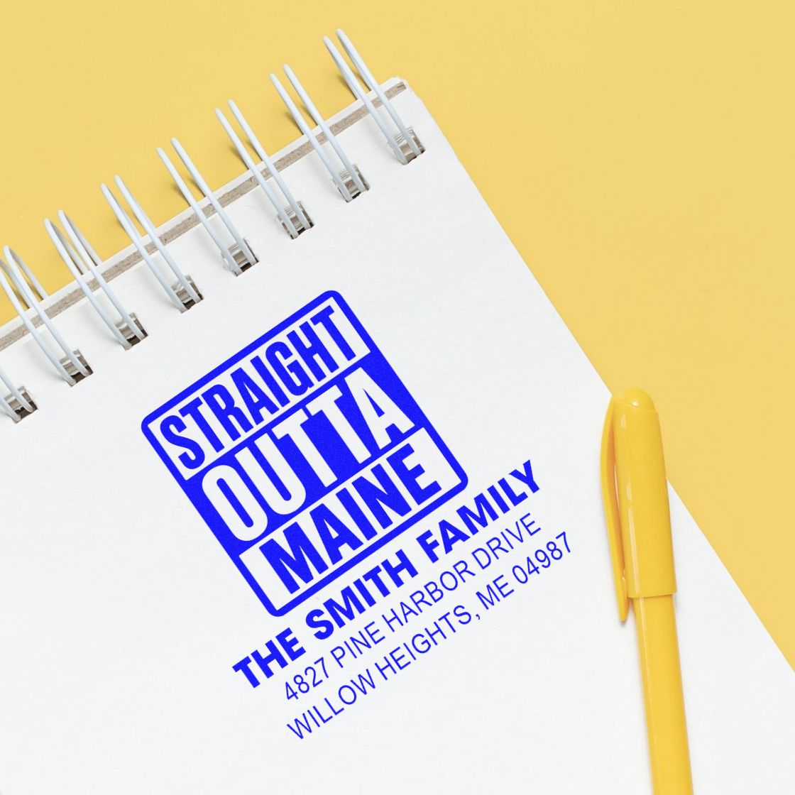Custom rubber stamp mockup reading Straight Outta Maine with Smith family address on a notebook beside a yellow pen.