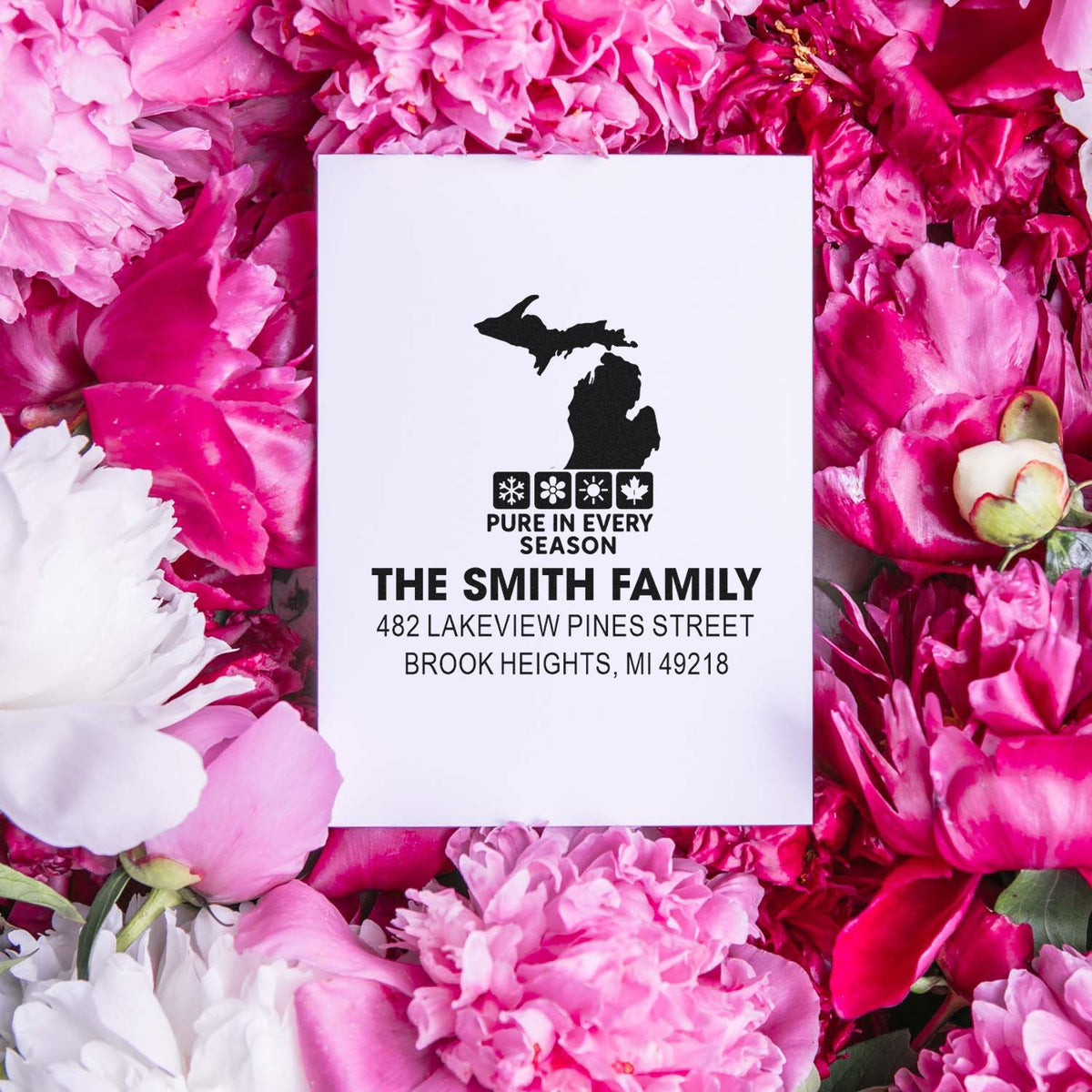 Personalized Michigan address rubber stamp mockup with family name, seasonal icons, and pink floral background.