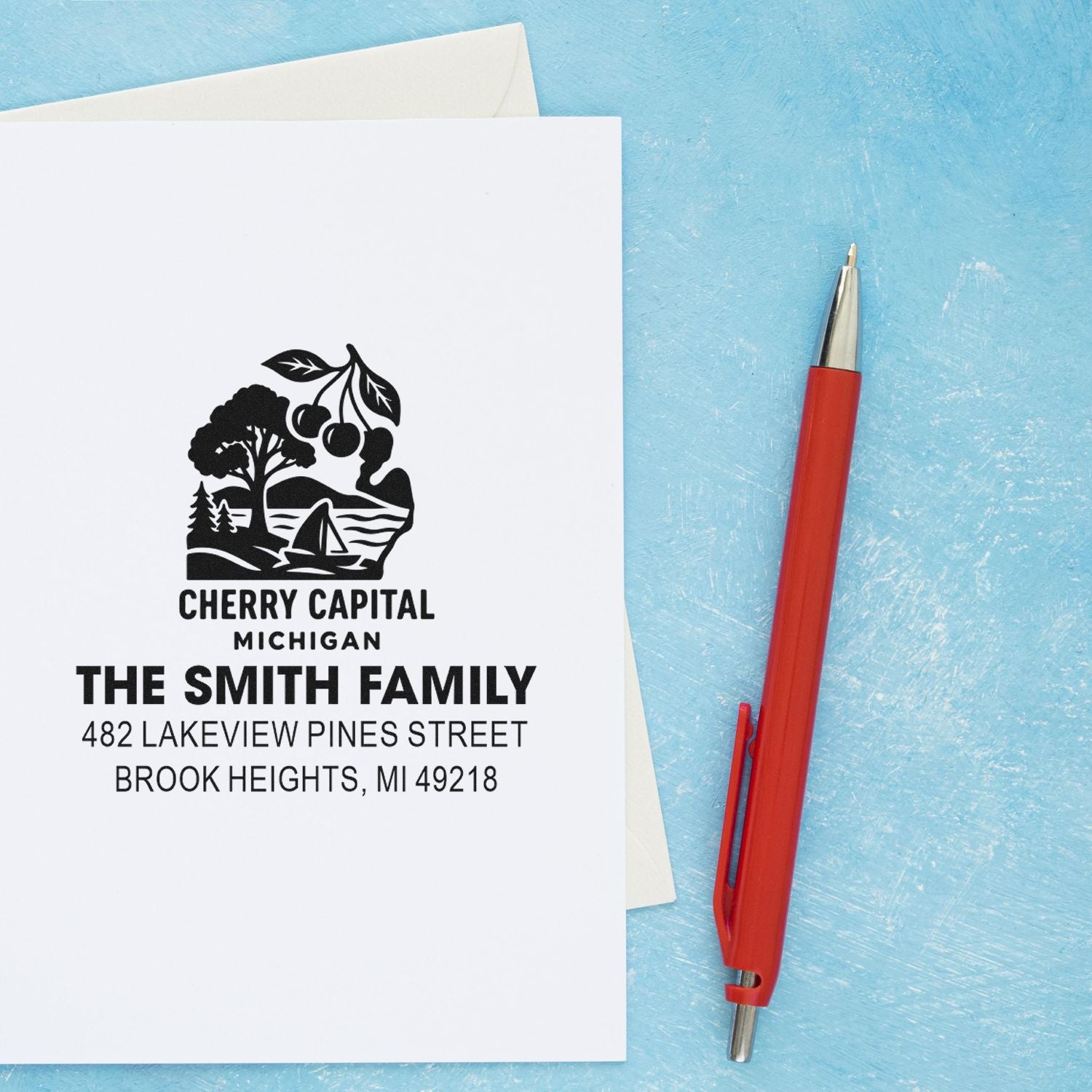 Custom address rubber stamp with family name and Michigan return address on stationery, shown beside a red pen.