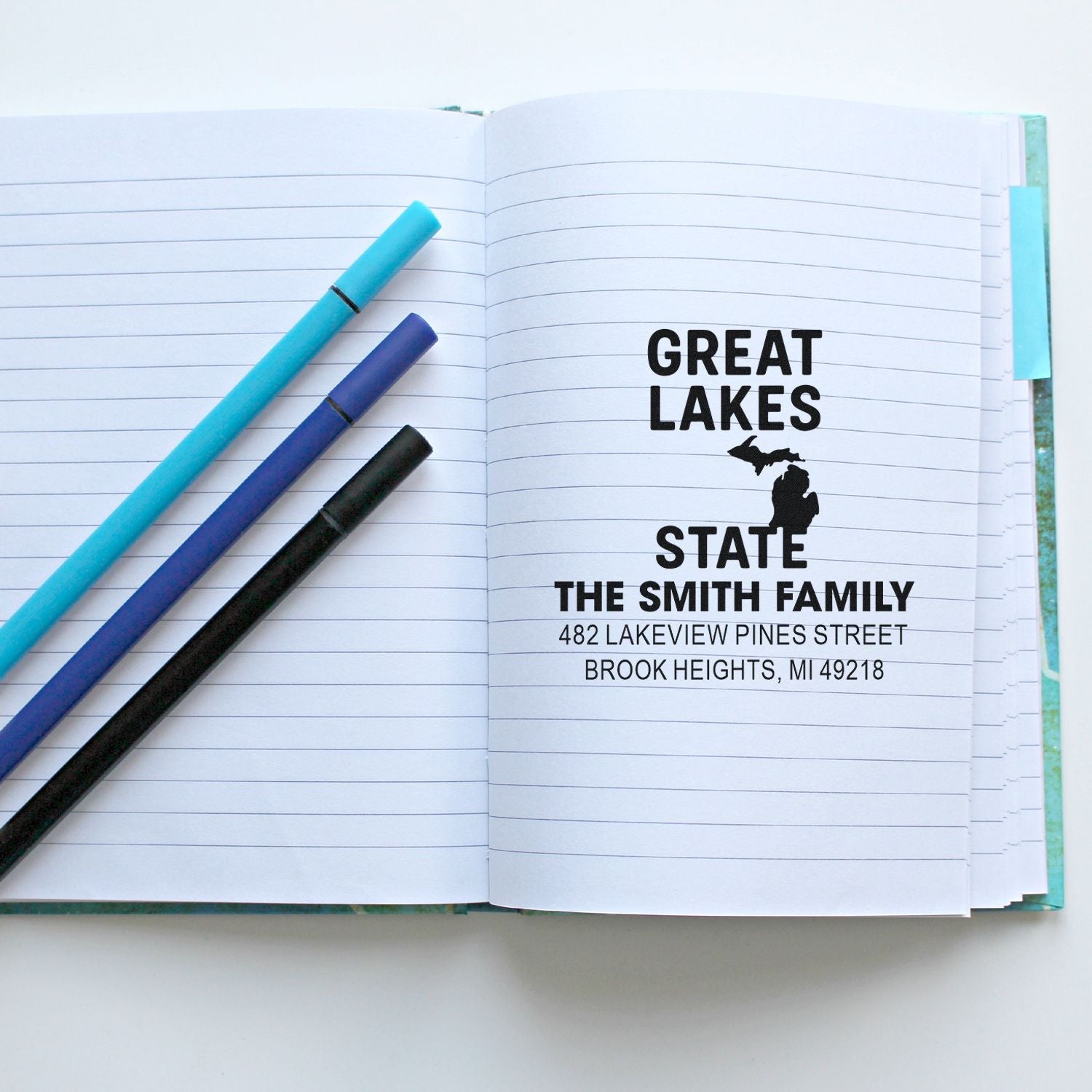 Personalized Great Lakes State return address rubber stamp on notebook page with pens, ideal for custom stationery.