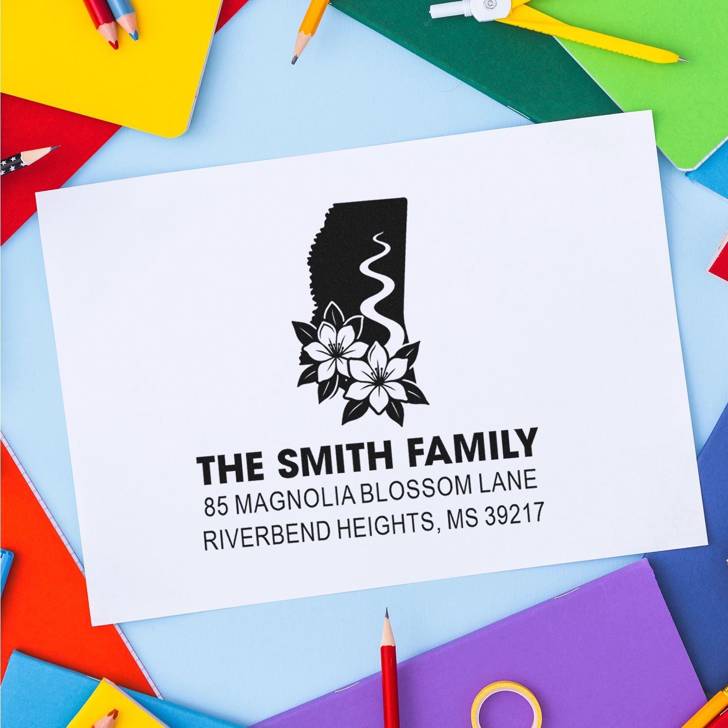 Personalized family return address rubber stamp imprint on a white envelope, surrounded by colorful stationery.