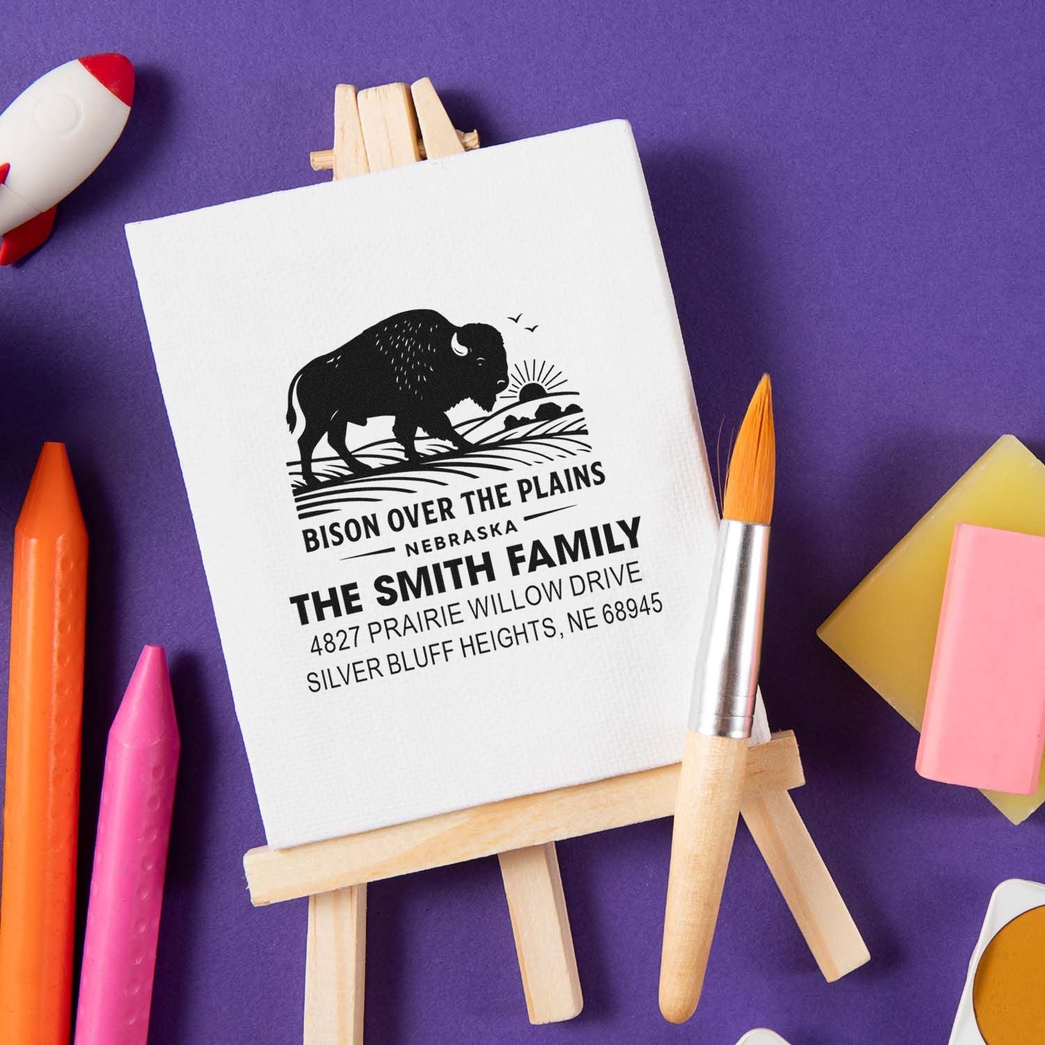 Custom bison return address rubber stamp for The Smith Family, Nebraska, shown on a mini easel with art supplies.