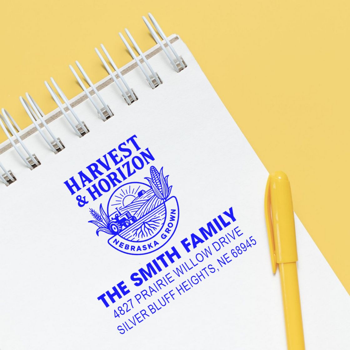 Custom family address rubber stamp with Nebraska return address, stamped on a notebook beside a yellow pen.