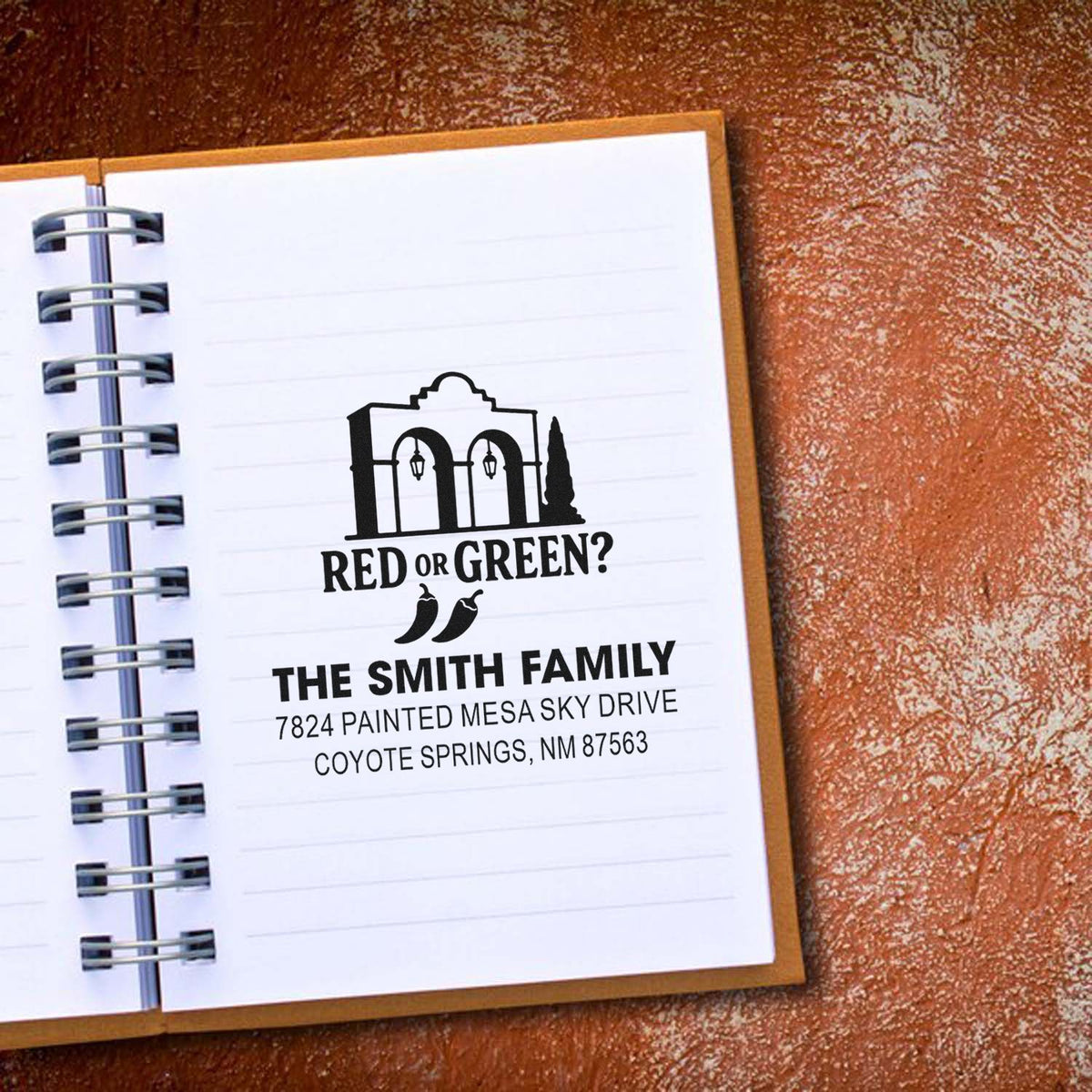 Custom rubber return address stamp with family name, address, and New Mexico-themed Red or Green? design on a notebook page.