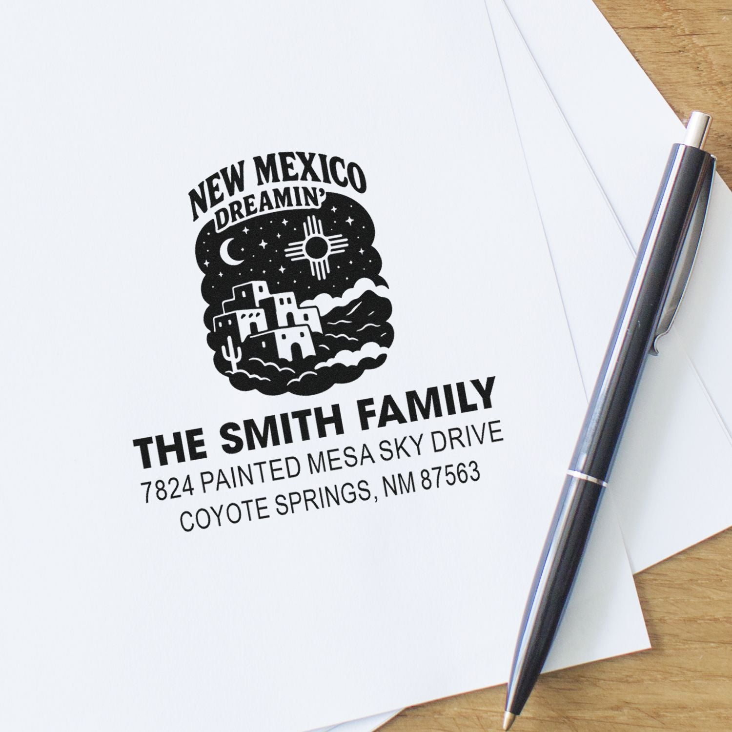 Custom return address rubber stamp for The Smith Family with New Mexico design, stamped on paper with a pen nearby.