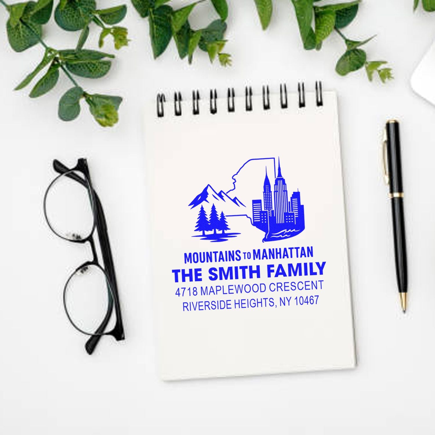 Custom rubber stamp on notebook featuring a Mountains to Manhattan family return address with skyline and mountain logo.