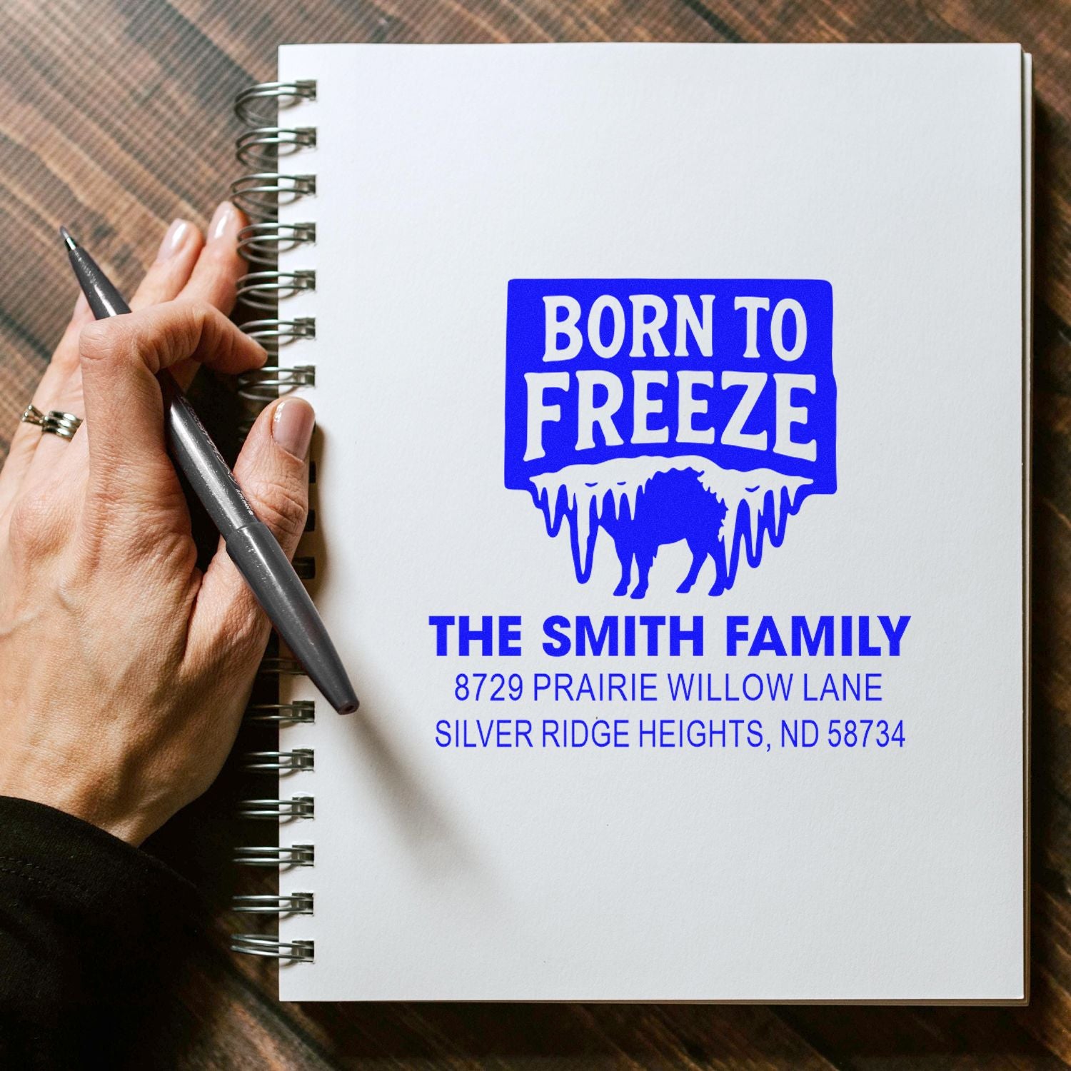 Custom rubber stamp impression reading Born to Freeze with family name and address on a notebook.