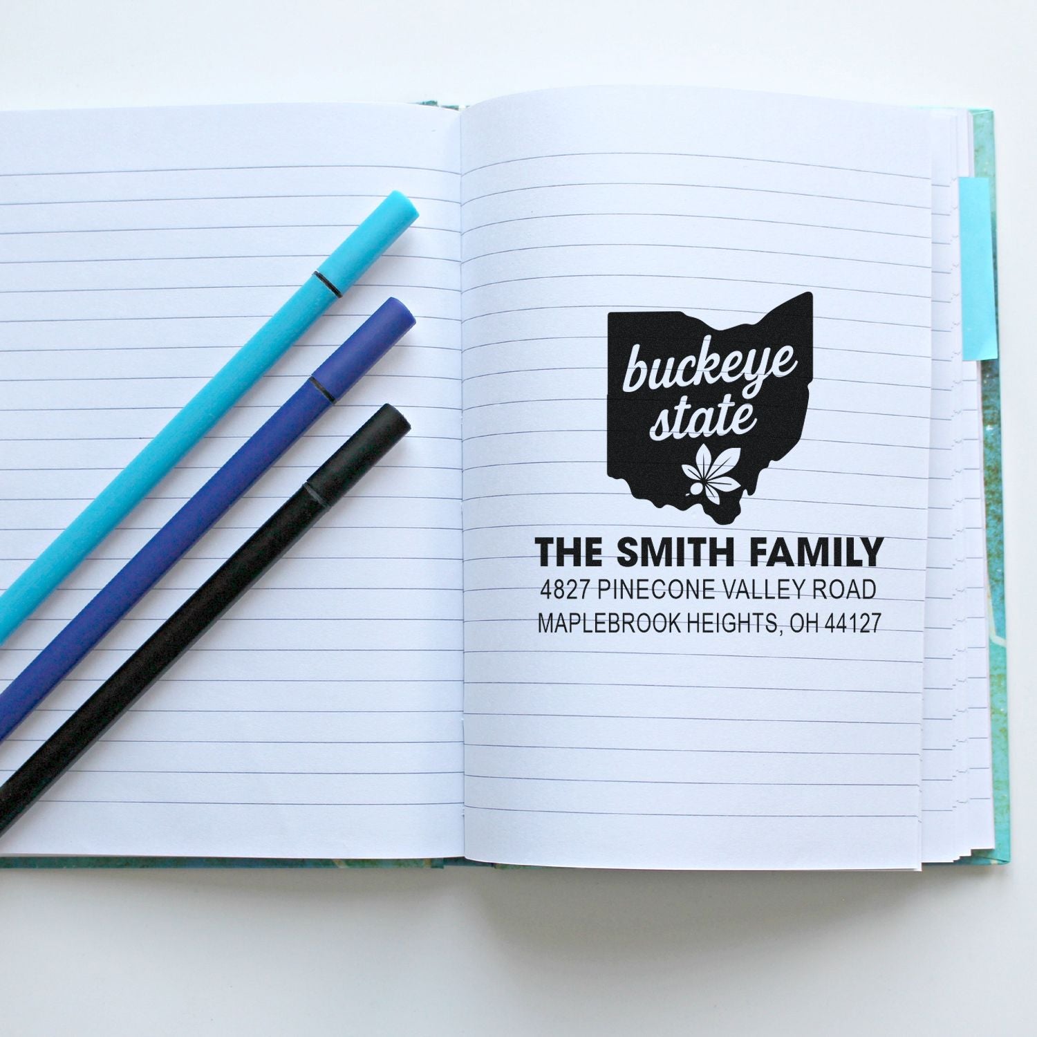 Personalized Buckeye State return address rubber stamp with family name and Ohio address on a lined notebook.