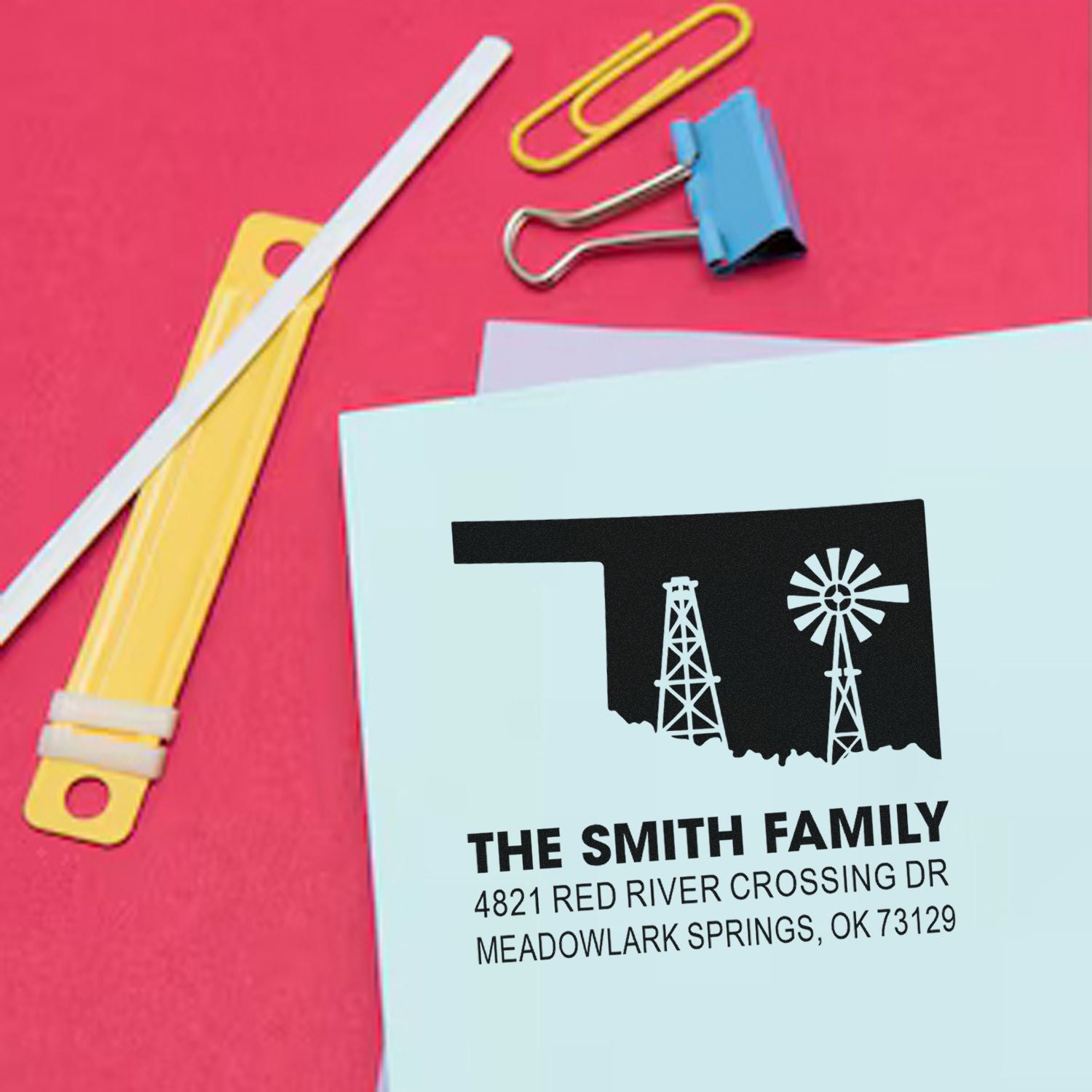 Custom rubber stamp return address design with oil rig and windmill logo on envelope, with stationery on pink background.