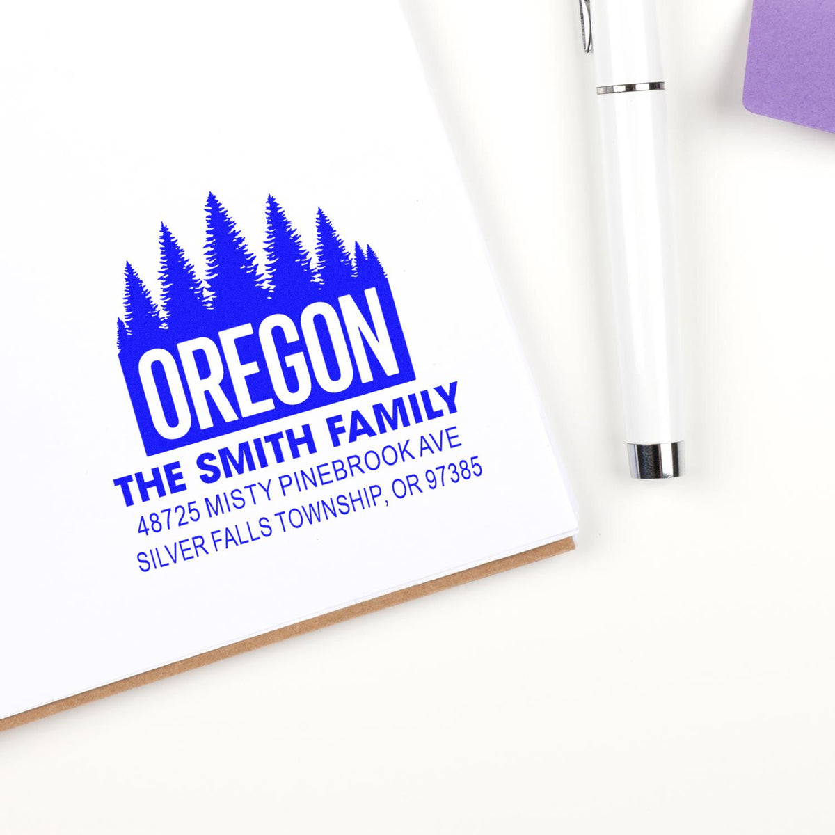Custom Oregon return address rubber stamp imprint for The Smith Family on a notebook beside a pen.
