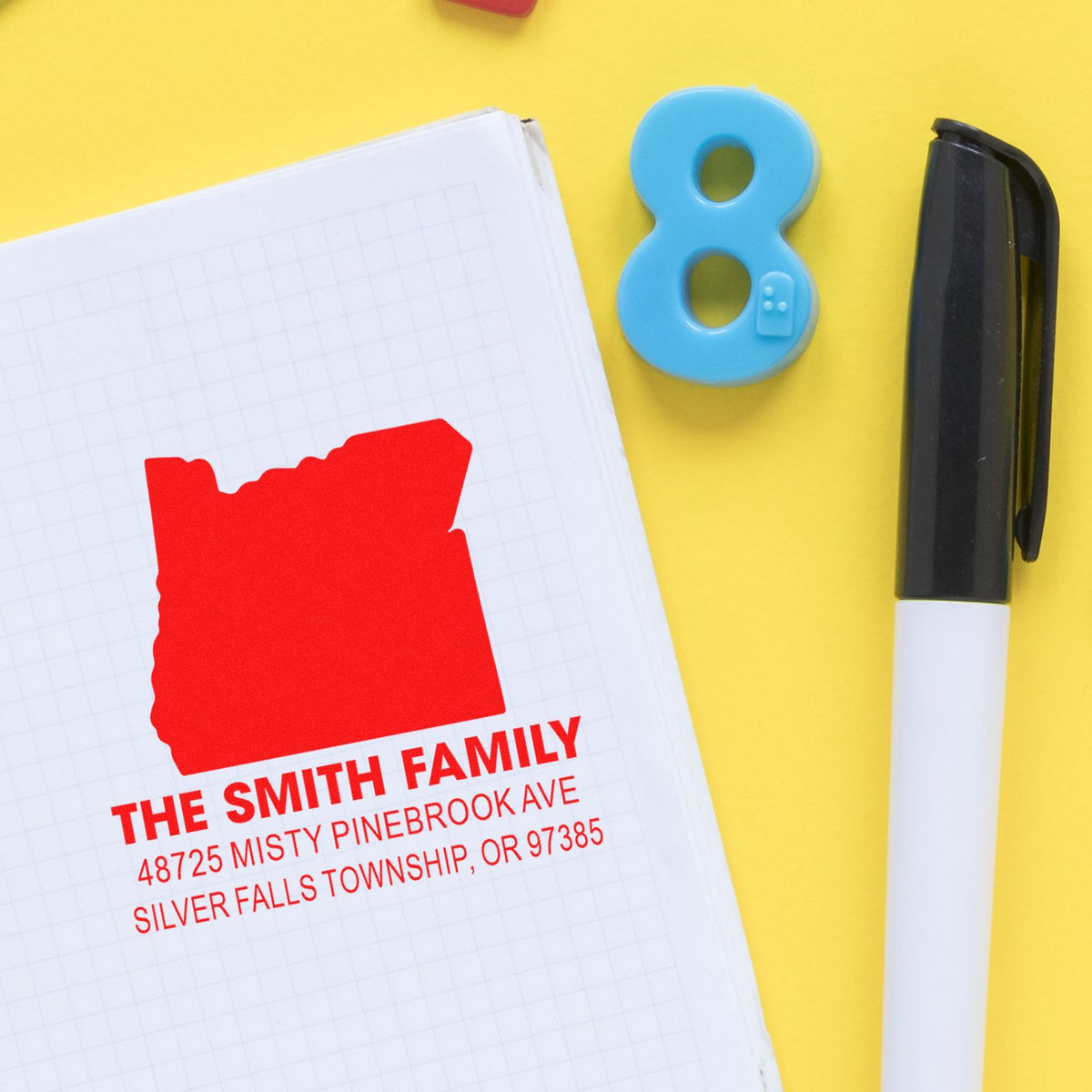 Custom return address rubber stamp impression for The Smith Family on notebook, with marker and number 8 on a yellow background.