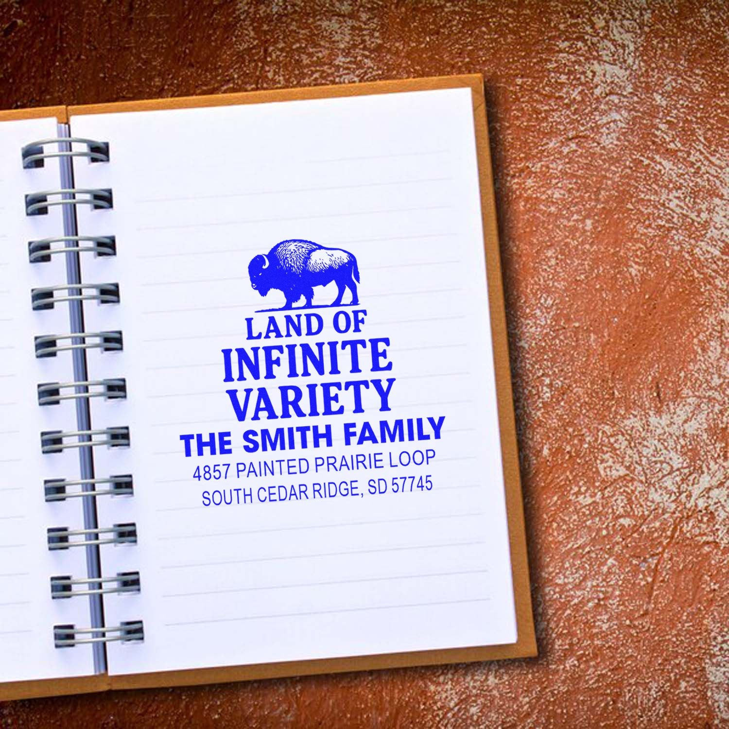 Personalized rubber address stamp with buffalo logo, family name, and South Dakota address, shown in a notebook.