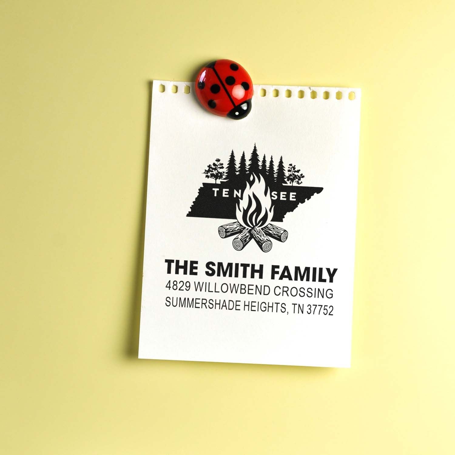 Custom Tennessee family address rubber stamp with campfire forest design on notepad, clipped with ladybug paperclip.
