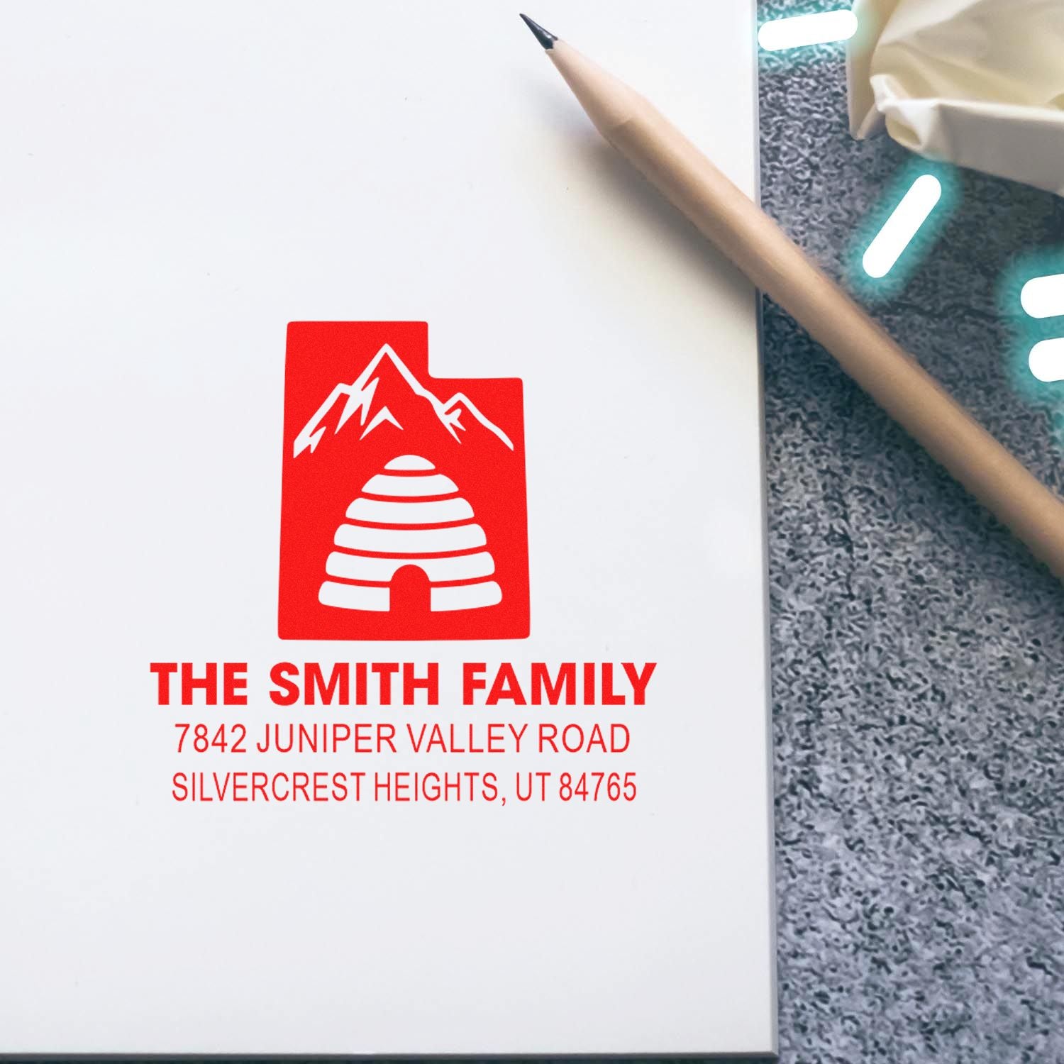 Custom family return address rubber stamp with mountain and igloo logo, shown in red on white paper.