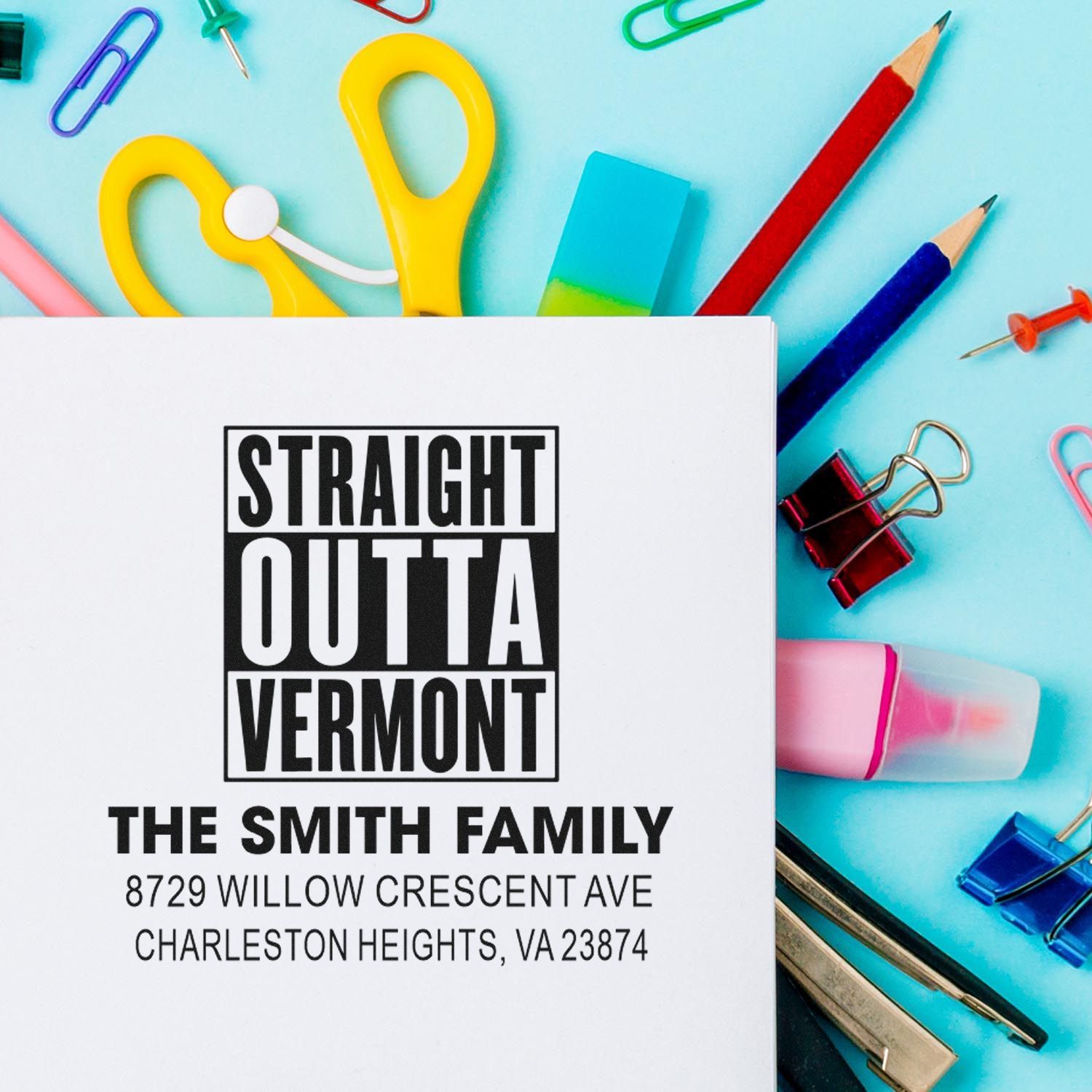 Custom address stamp reading Straight Outta Vermont for The Smith Family, styled with colorful stationery, pencils, clips, and scissors on a blue desk.