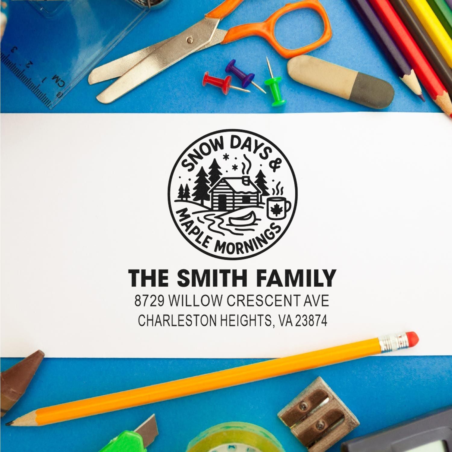 Custom address stamp with Snow Days & Maple Mornings cabin logo for The Smith Family, surrounded by school supplies on a blue background.