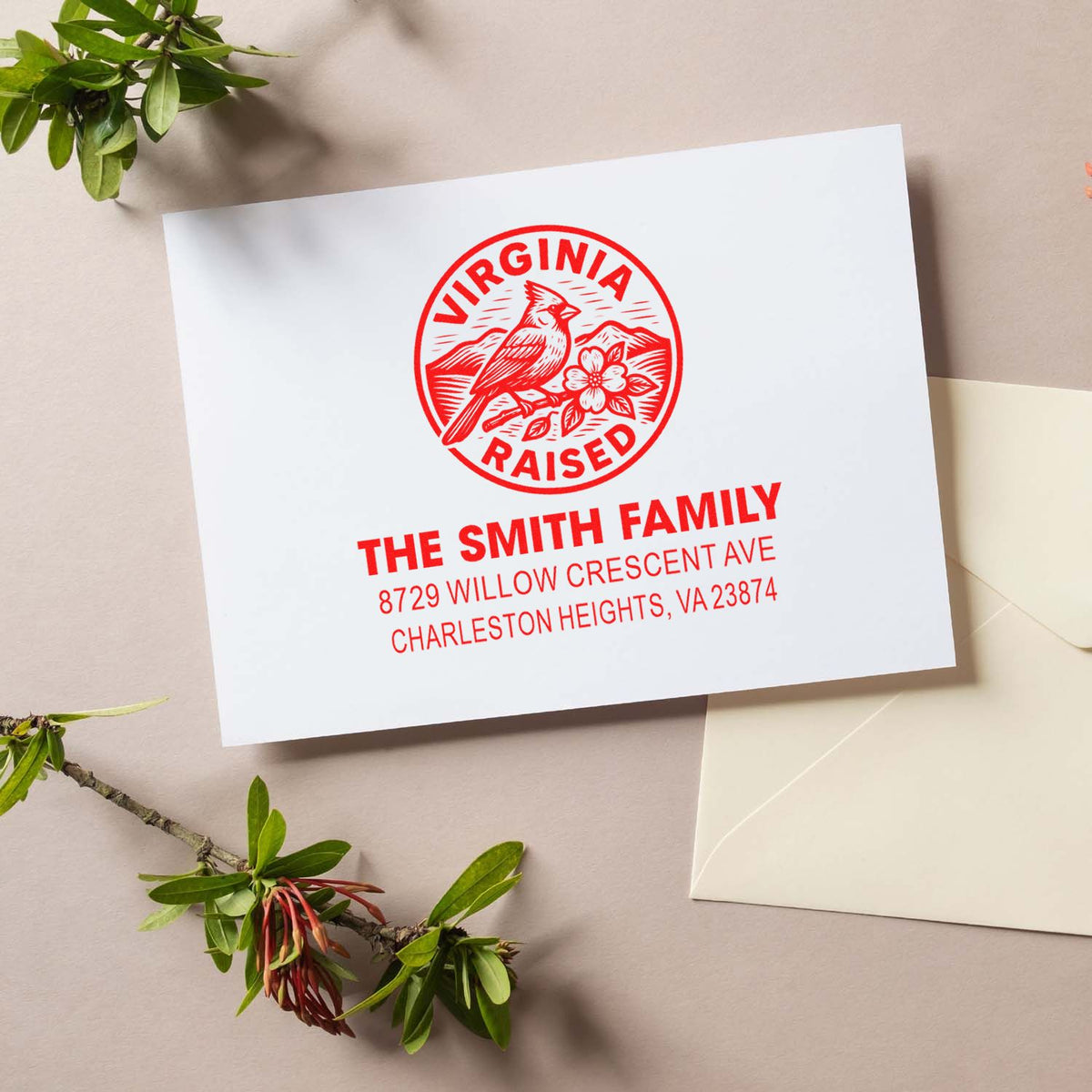 Custom Virginia Raised address stamp on white card with red cardinal design, beside an envelope and greenery on a neutral tabletop.