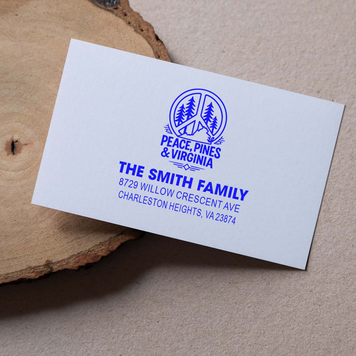 Blue custom return address stamp on a white card, featuring Peace, Pines & Virginia and The Smith Family, on a rustic wood slice.