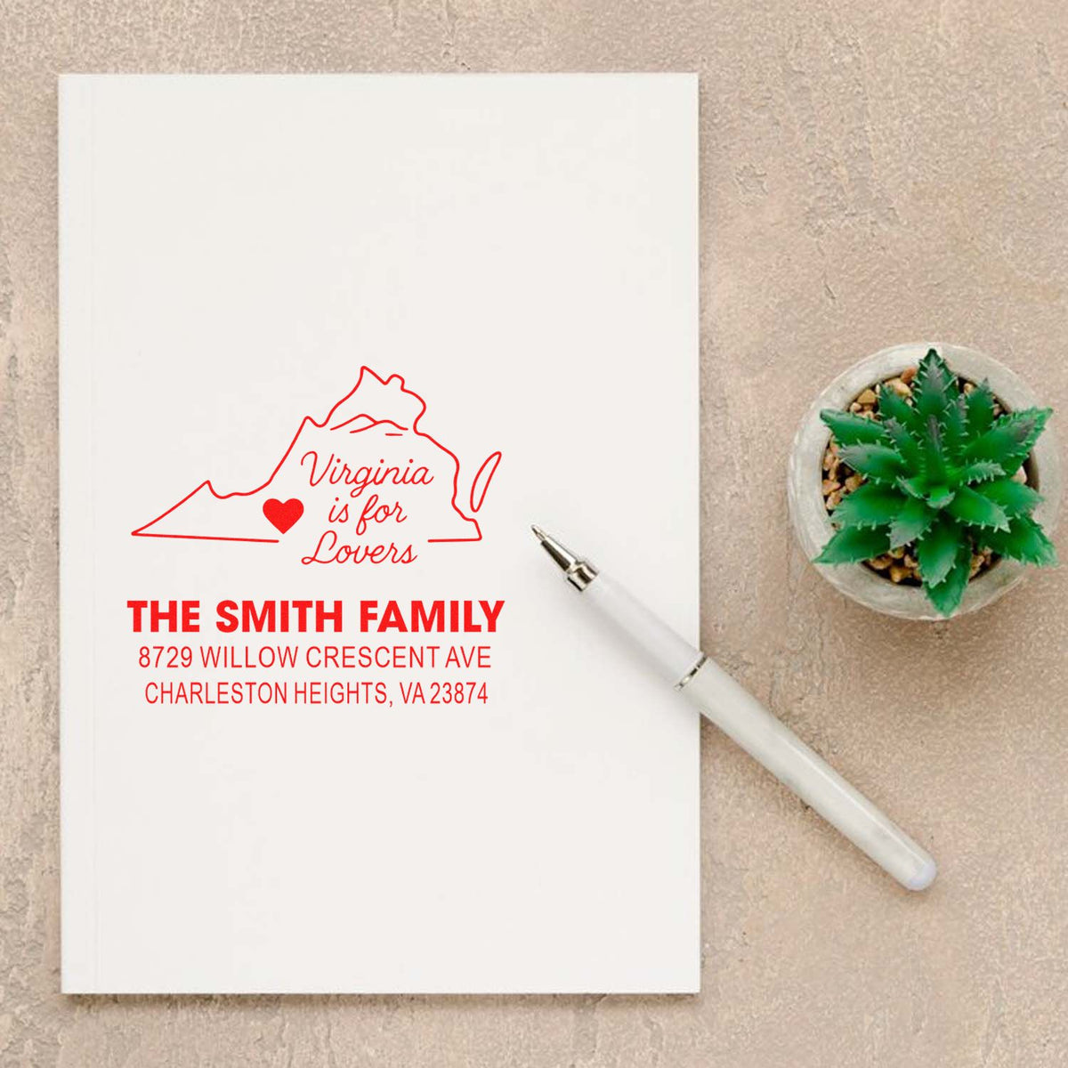 Custom Virginia is for Lovers address stamp with The Smith Family name, shown on a notebook beside a white pen and succulent on a desk.