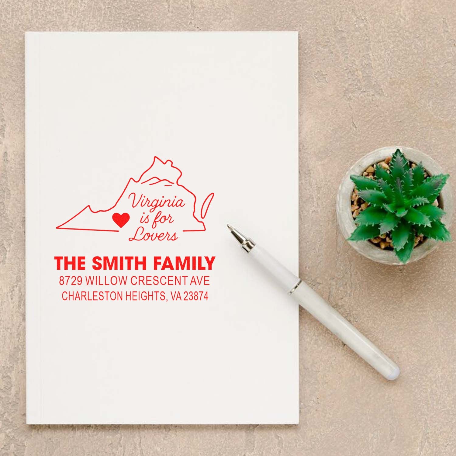 Custom Virginia address stamp with Virginia is for Lovers map design on white paper, beside a pen and potted succulent on a beige tabletop.